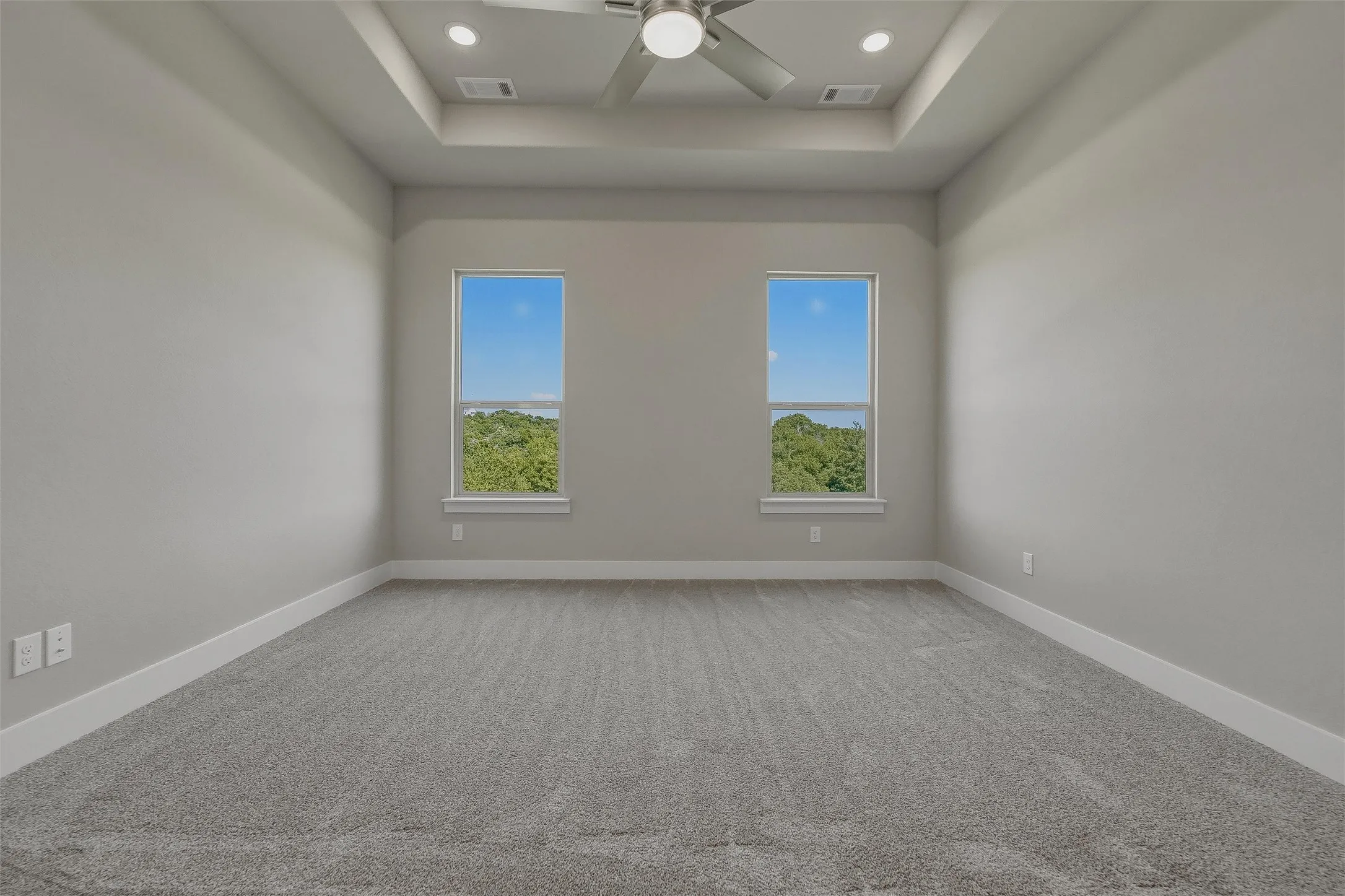 Tray ceiling with recessed lighting and a ceiling fan, dual windows, and plush carpeting
