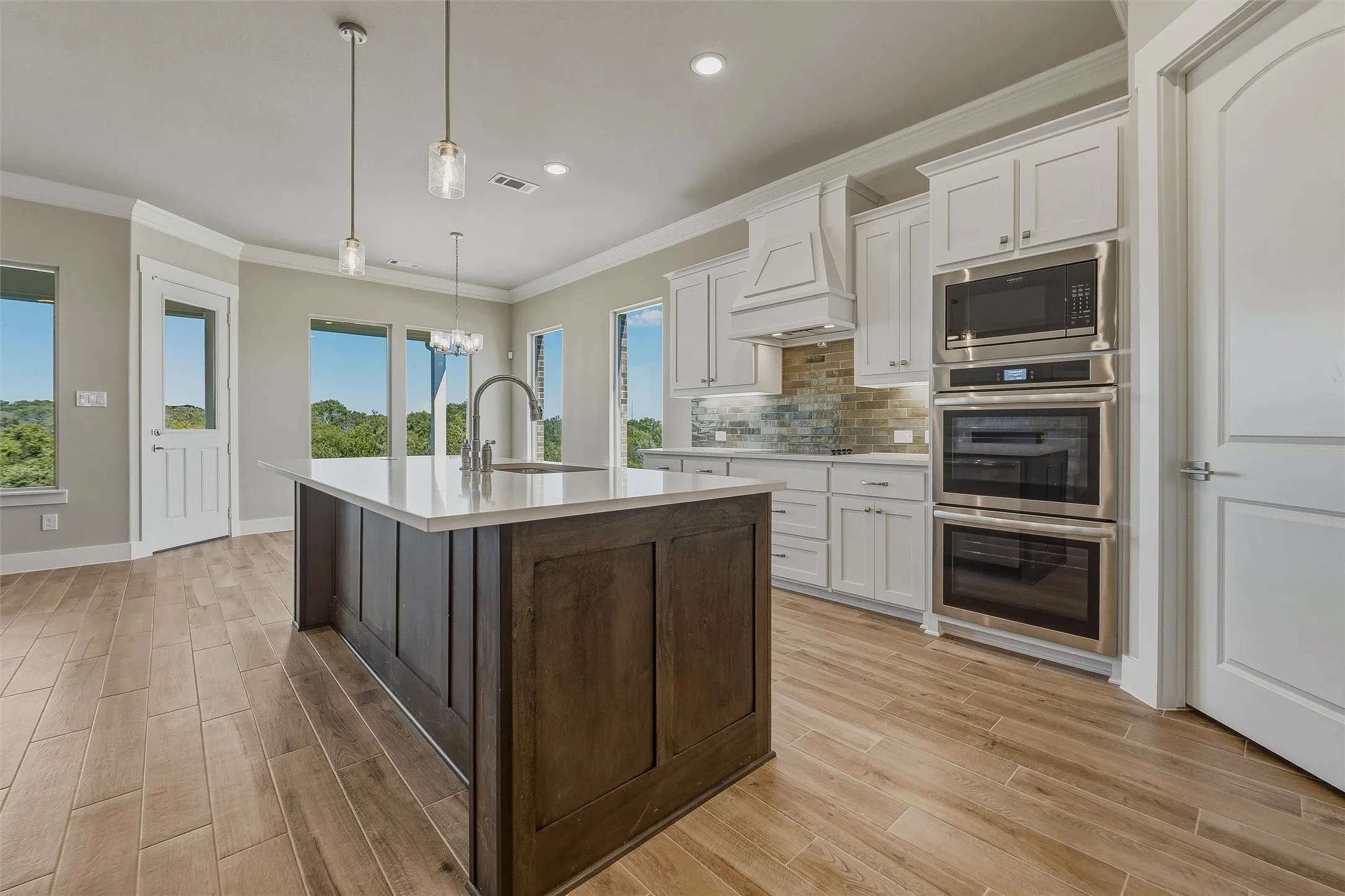 Kitchen featuring wood-finish flooring, a central island with a sink, white cabinetry, a built-in double oven, and stainless steel appliances