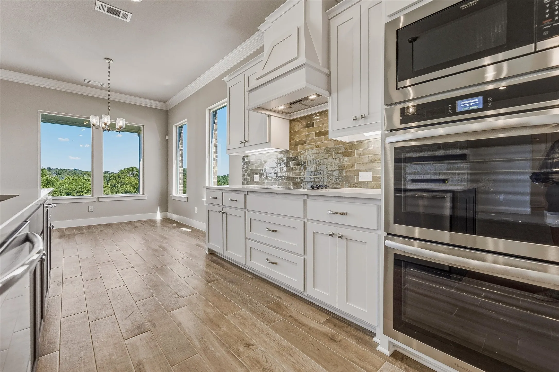 Gourmet kitchen featuring stainless steel double ovens, built-in microwave, white shaker cabinetry, and wood-finish flooring