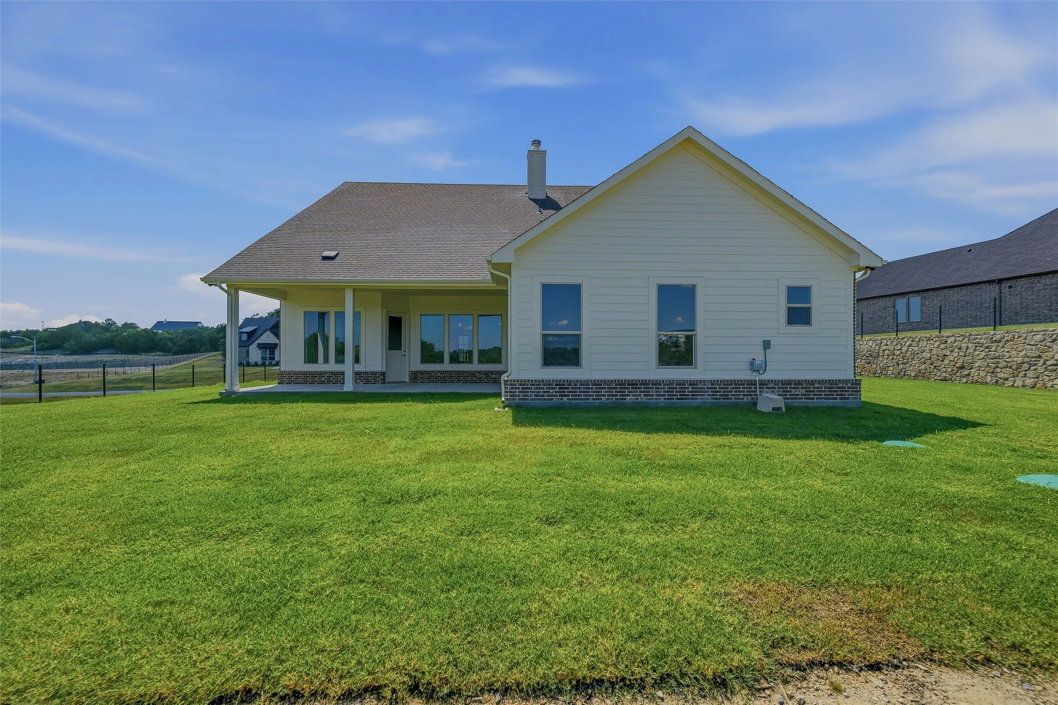 Rear elevation with a covered patio, extensive grass lawn, and brick and siding exterior