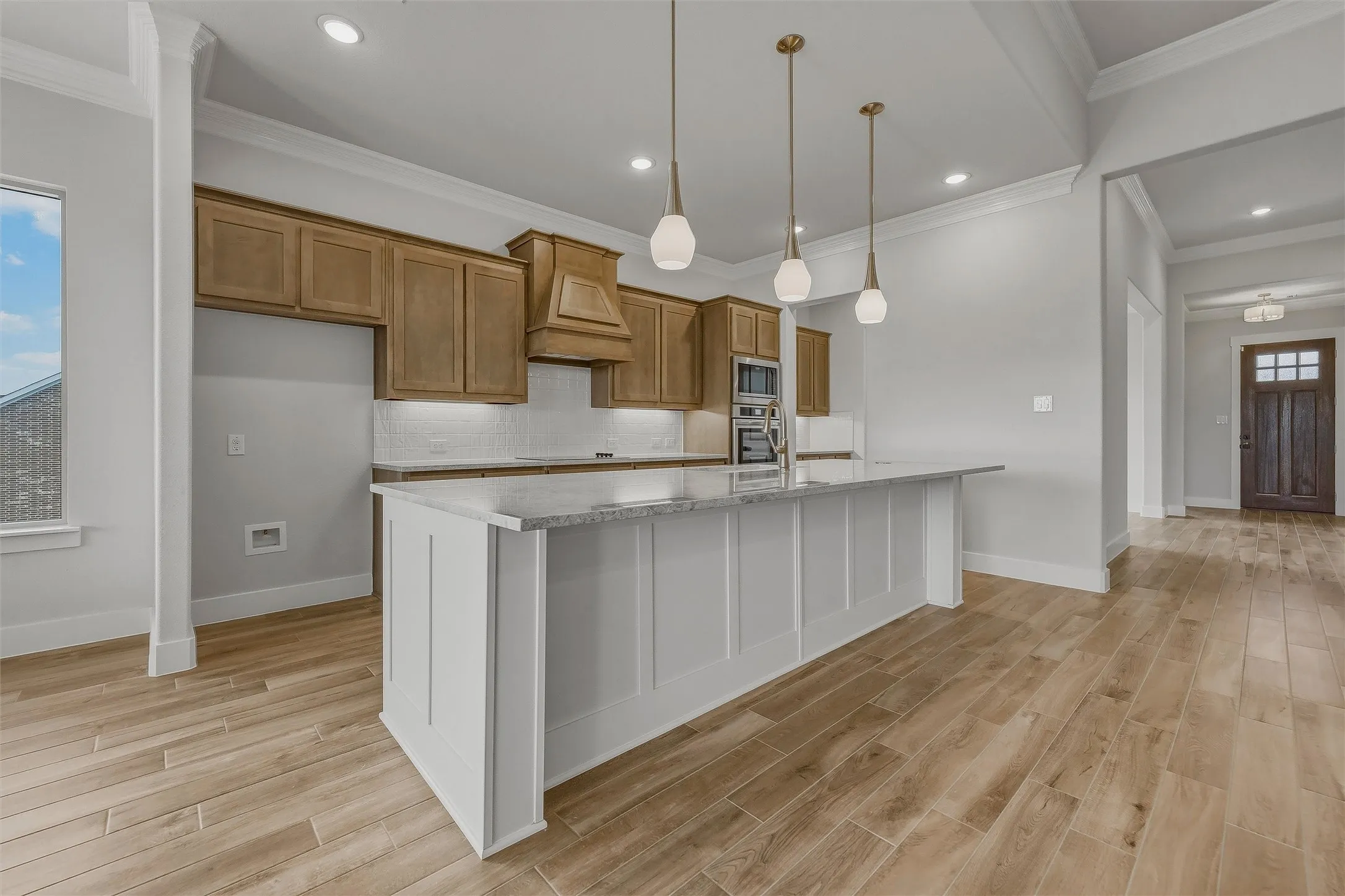 Expansive kitchen island with a stone countertop, overhead pendant lighting, and wood-finish flooring throughout
