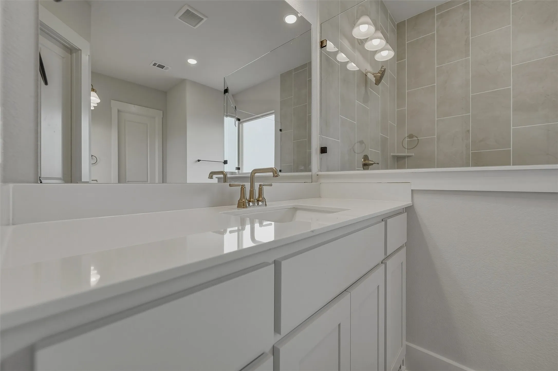 Integrated vanity with a single basin sink and brushed nickel faucet, large wall-mounted mirror, and tiled shower surround