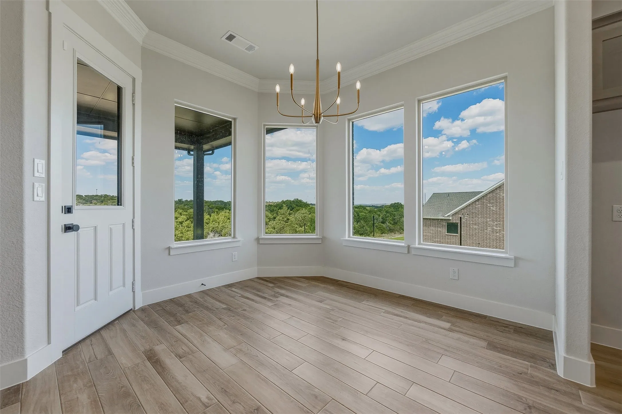 Wood-finish flooring, multiple windows, contemporary chandelier, crown molding, and a paneled door with glass insert
