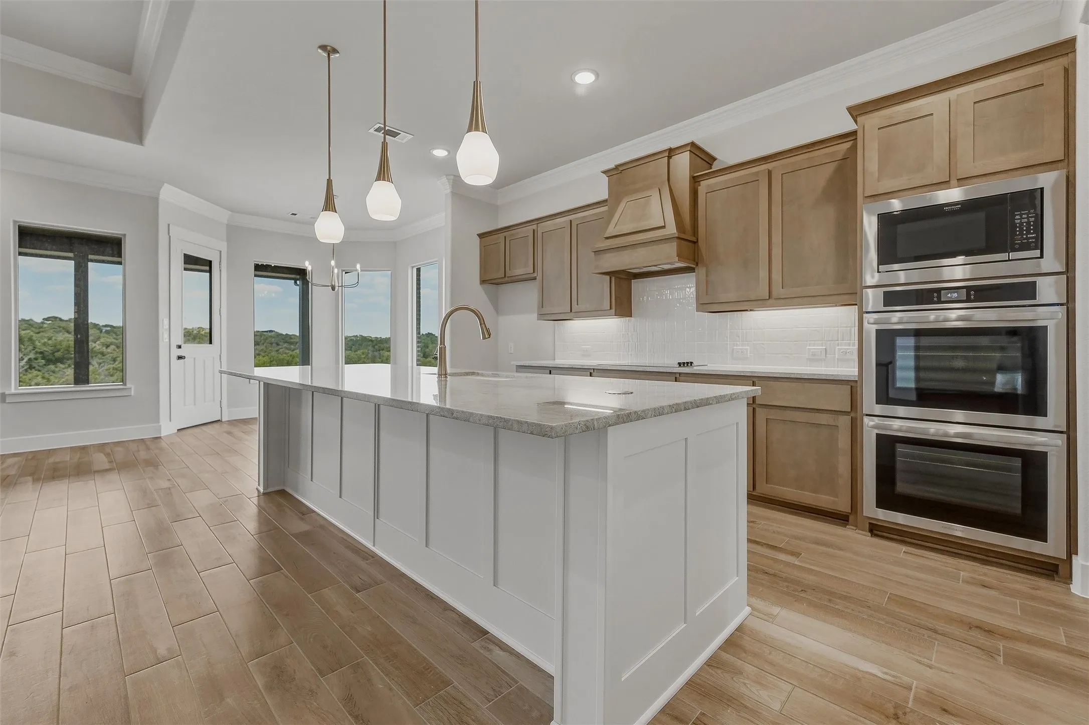 Gourmet kitchen featuring a large central island, stainless steel double ovens, a built-in microwave, wood-finish flooring, and ample natural light