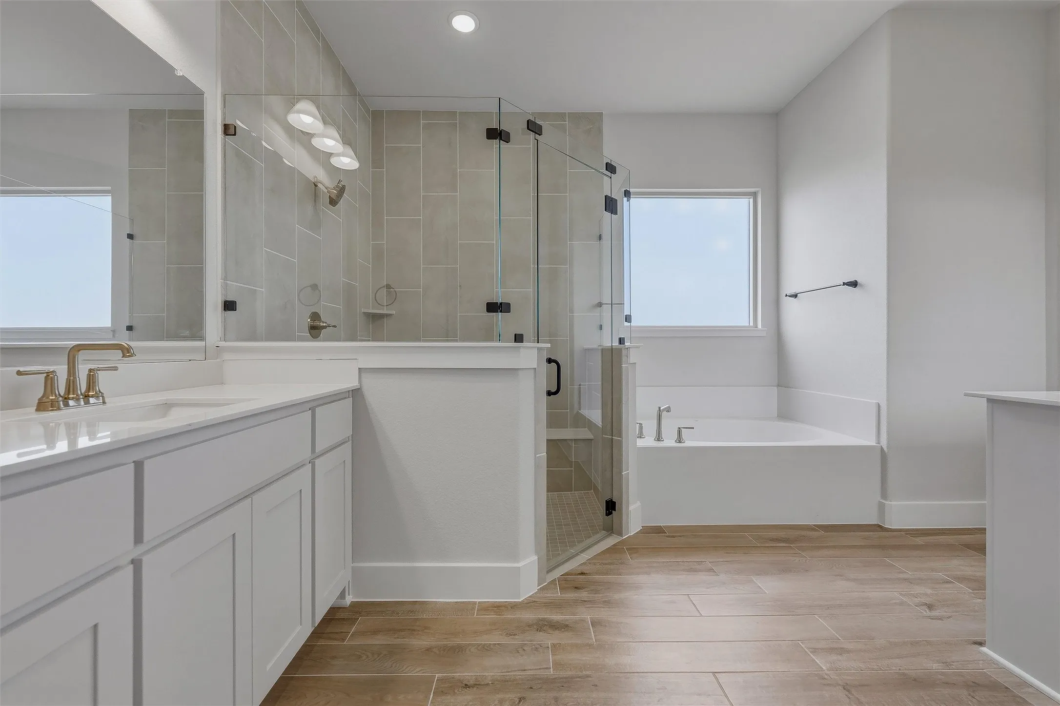Dual vanity with white cabinetry and integrated sinks, a walk-in shower with glass enclosure, a built-in soaking tub, and wood-finish flooring