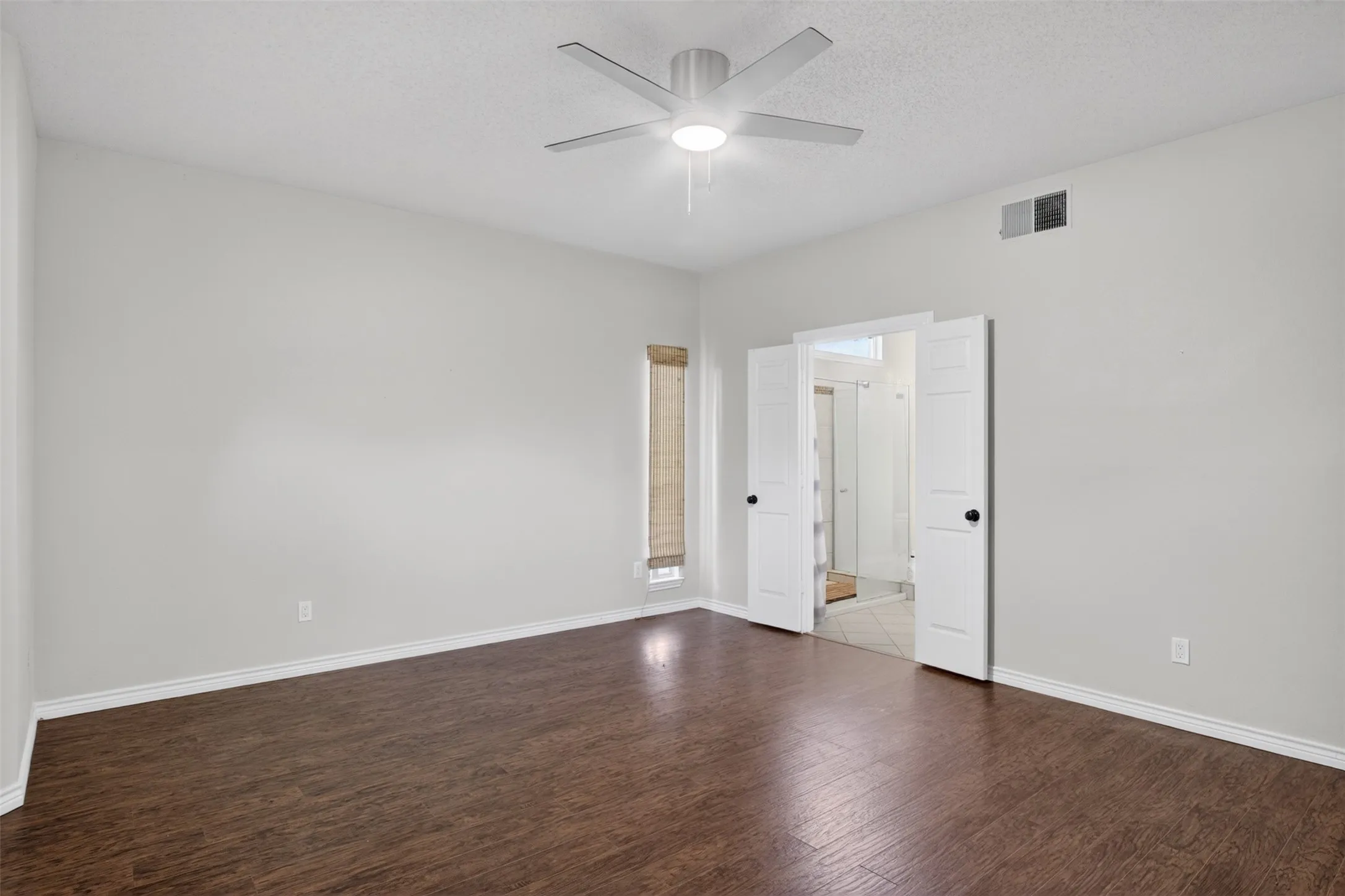 Spacious room featuring rich wood-toned flooring, light-colored walls, a ceiling fan, and a window with blinds