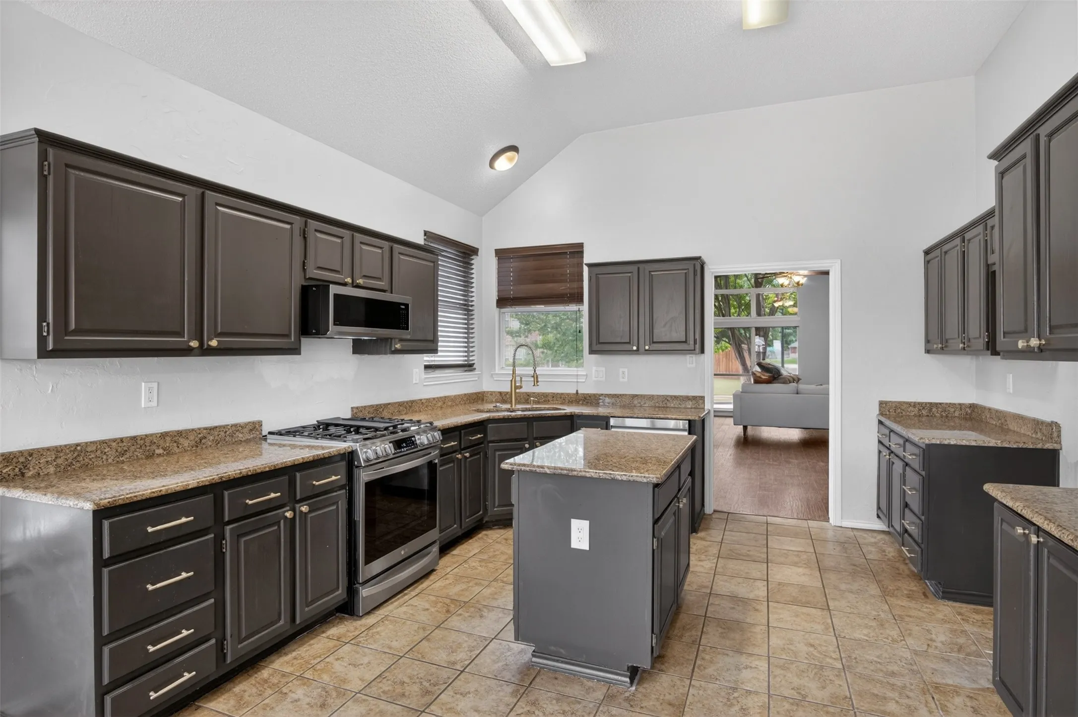 The kitchen features dark cabinetry, granite countertops, a central island, and tiled flooring