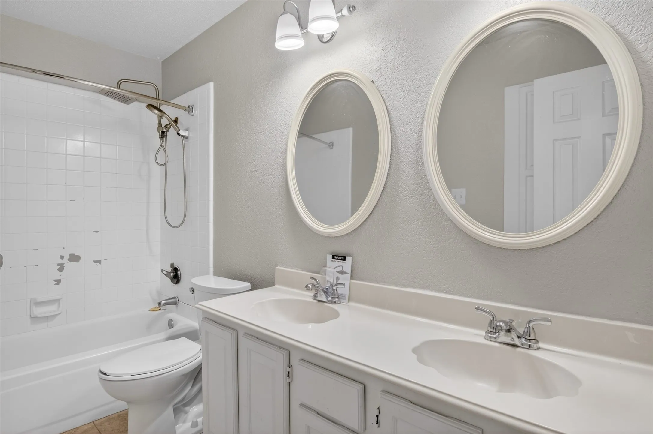 Bathroom featuring a dual vanity with two sinks, two mirrors, and a combination shower and bathtub