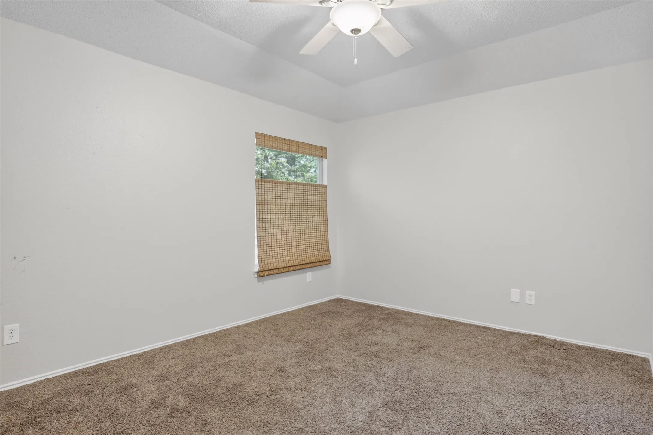 This room features carpeting, a window with a woven blind, and a ceiling fan with an integrated light fixture