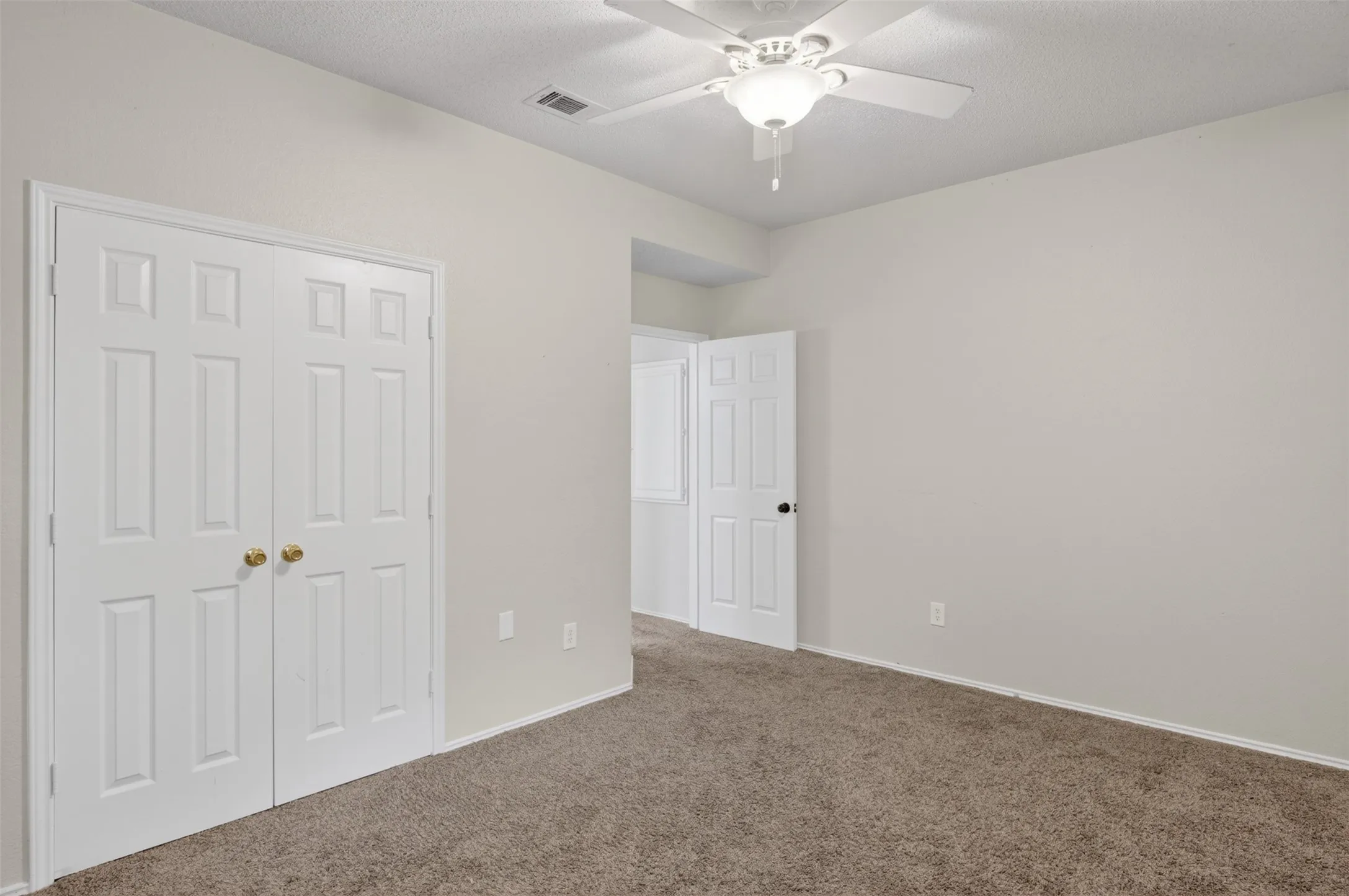 This room features light neutral-toned walls, carpeted flooring, and a ceiling fan with integrated lighting