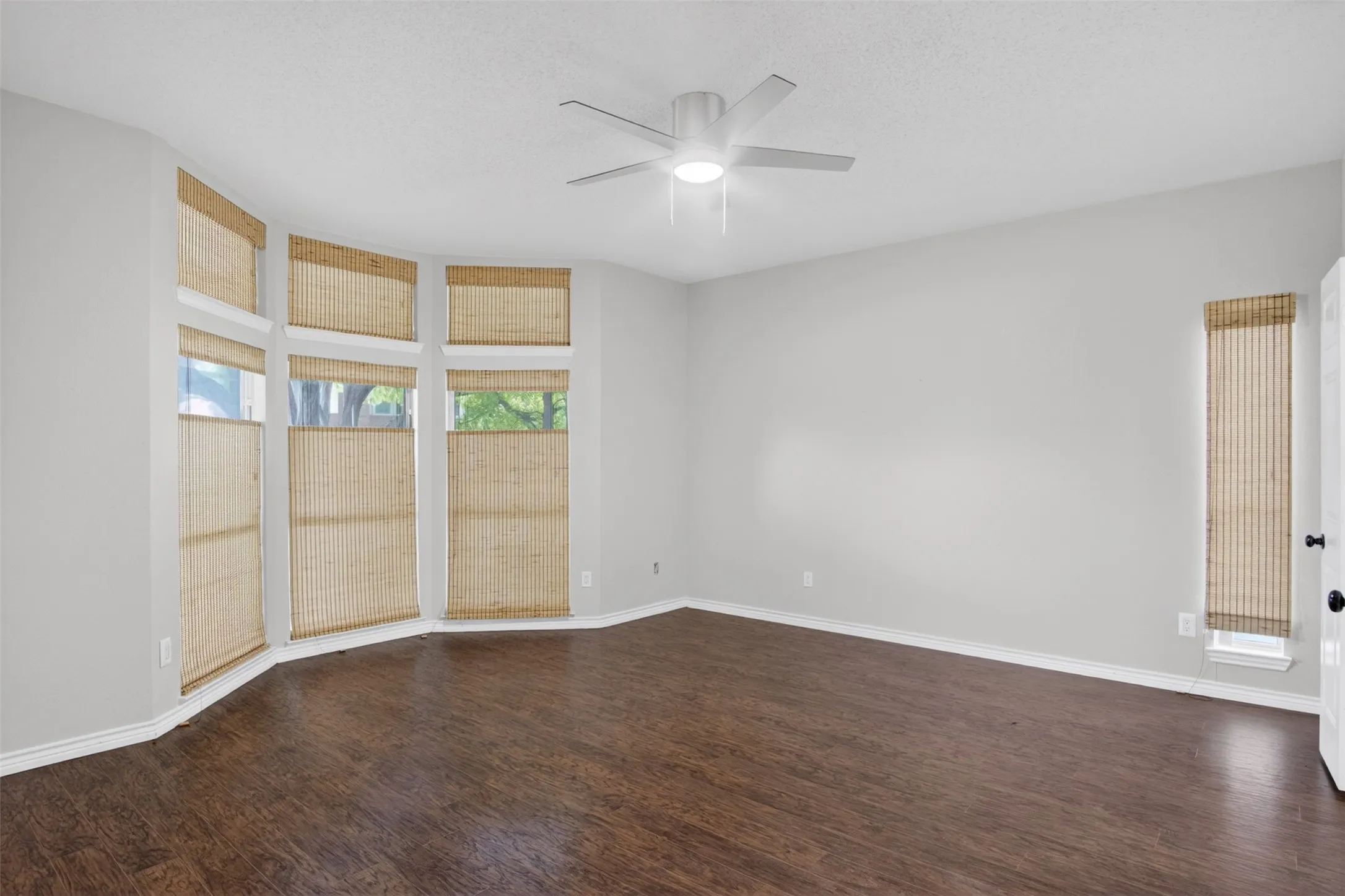 This room features wood flooring, a ceiling fan with integrated lighting, and a bay window with blinds