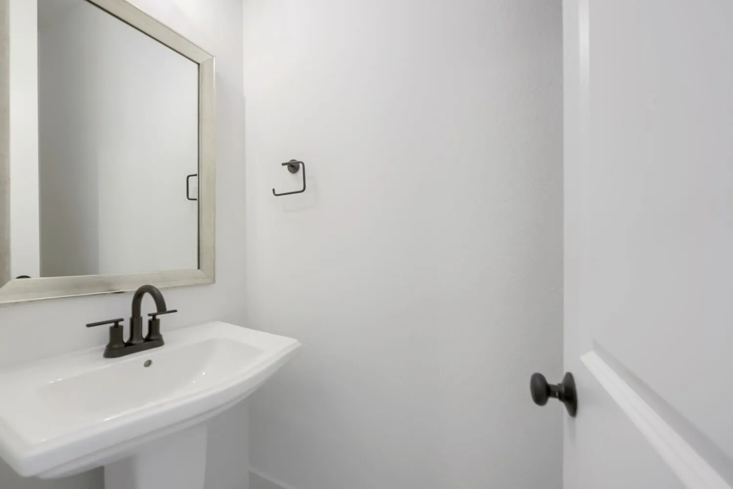 Pedestal sink featuring a dark bronze faucet, framed mirror with a distressed finish, and white walls
