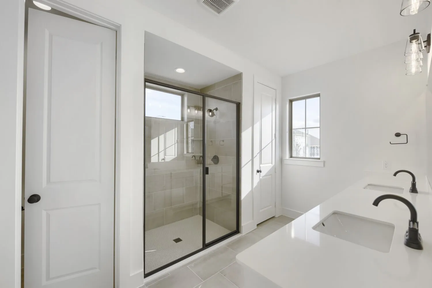 Bathroom featuring a frameless glass shower enclosure with matte black trim, dual undermount sinks, and a white countertop