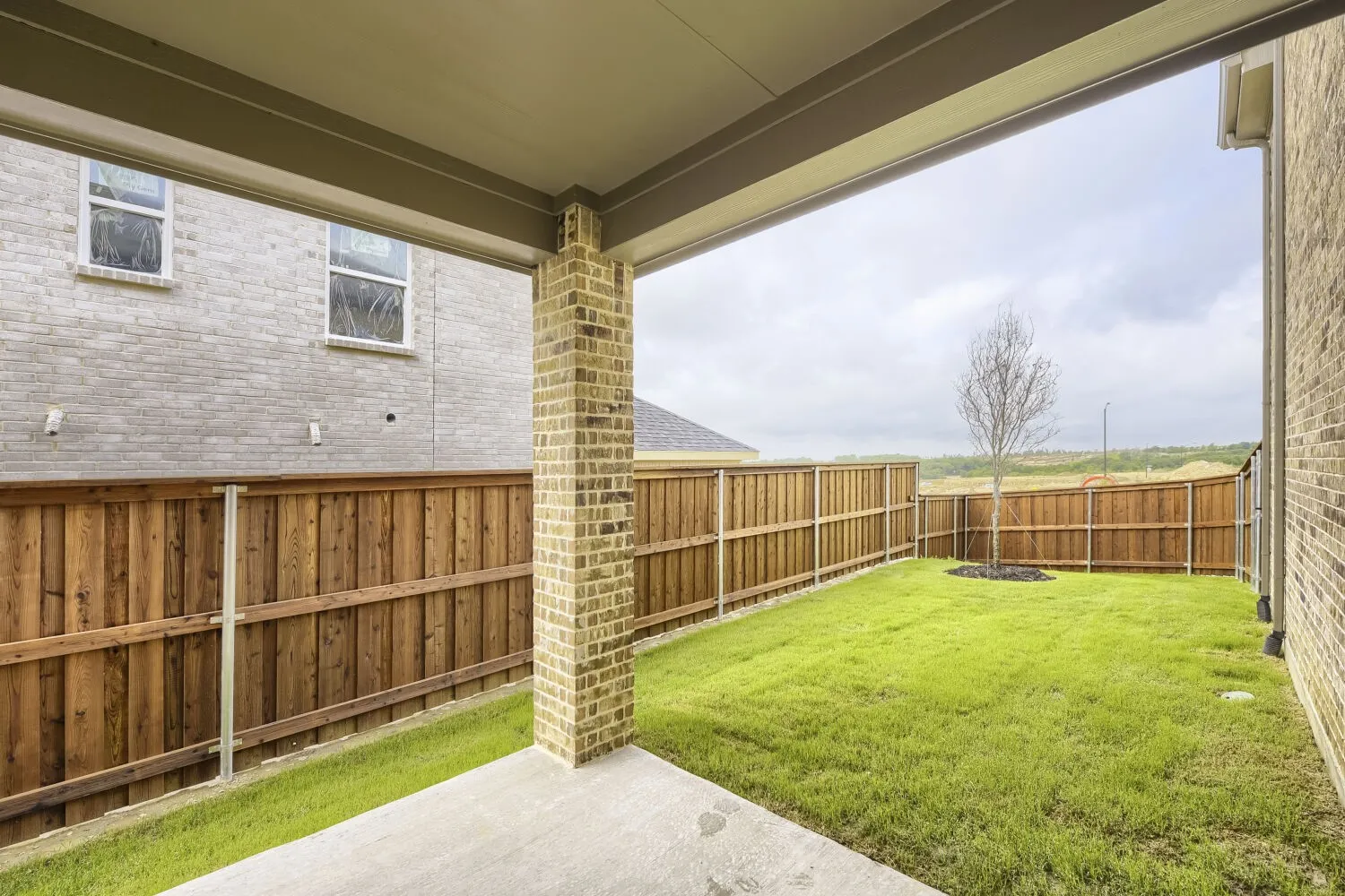 Covered patio with a concrete slab, brick support column, and light-colored brick exterior