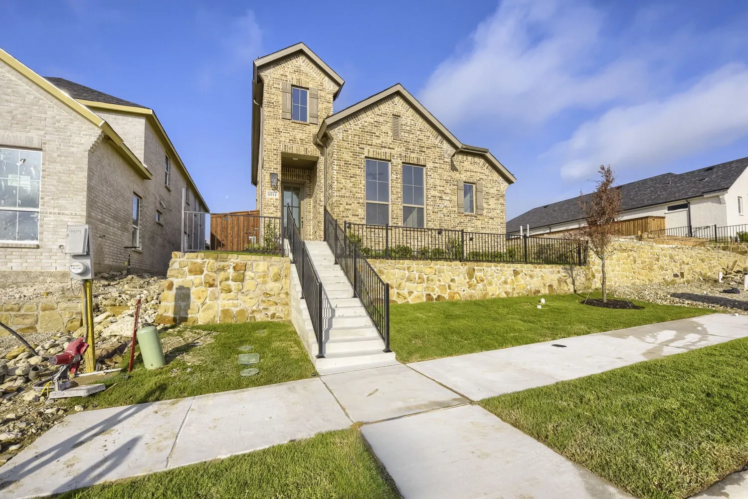 Two-story stone exterior featuring a prominent entryway tower, concrete walkway, and a landscaped front yard with a young tree