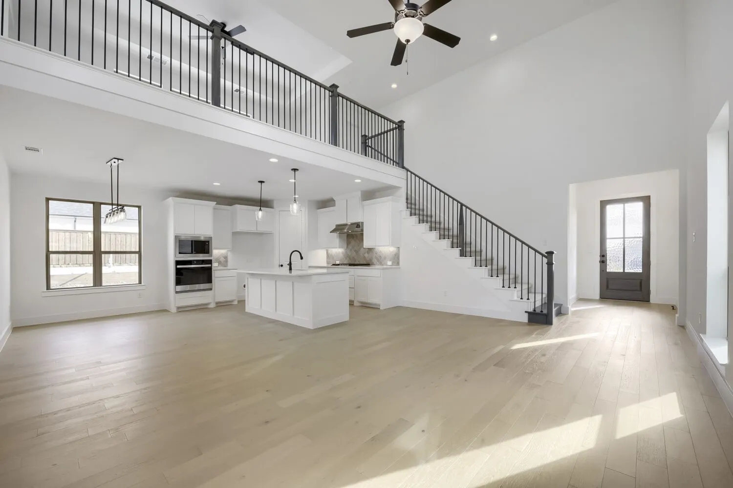 Open-concept living area featuring light wood-finish flooring, soaring ceilings, and a modern kitchen