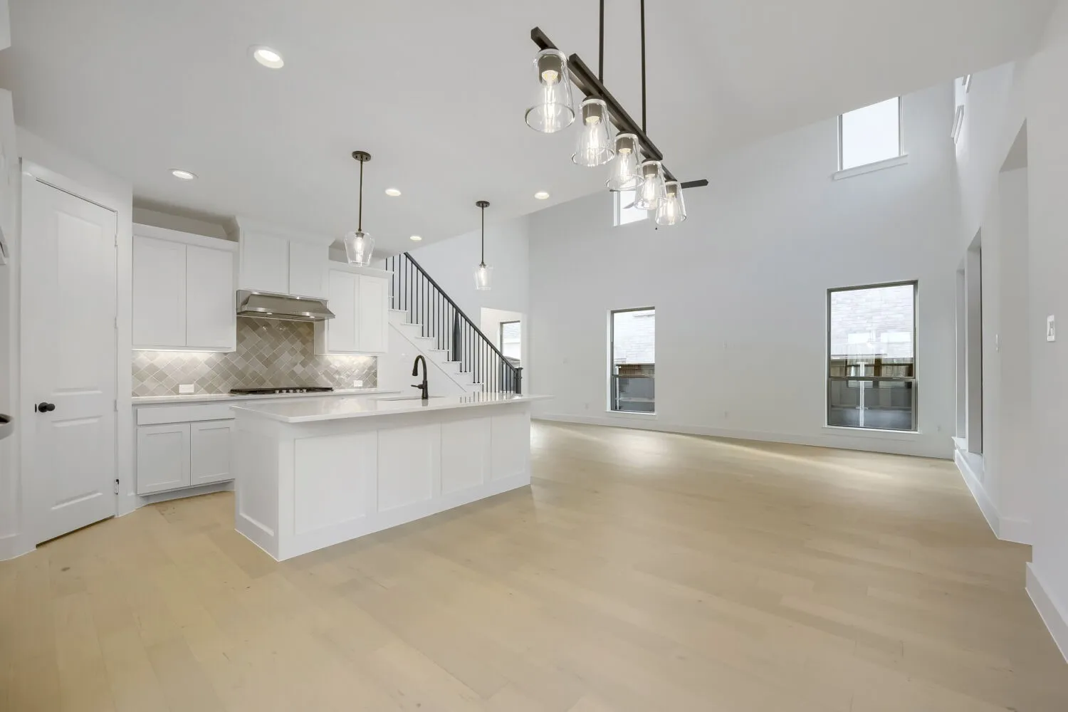 Open-concept living space featuring light wood-finish flooring, a white kitchen island with a dark faucet, a tiled backsplash, and recessed lighting