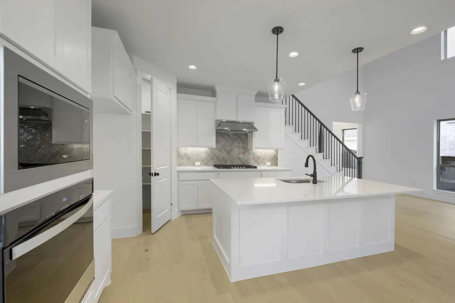 Modern kitchen featuring white cabinetry, a large center island with a built-in sink, stainless steel appliances, and wood-finish flooring