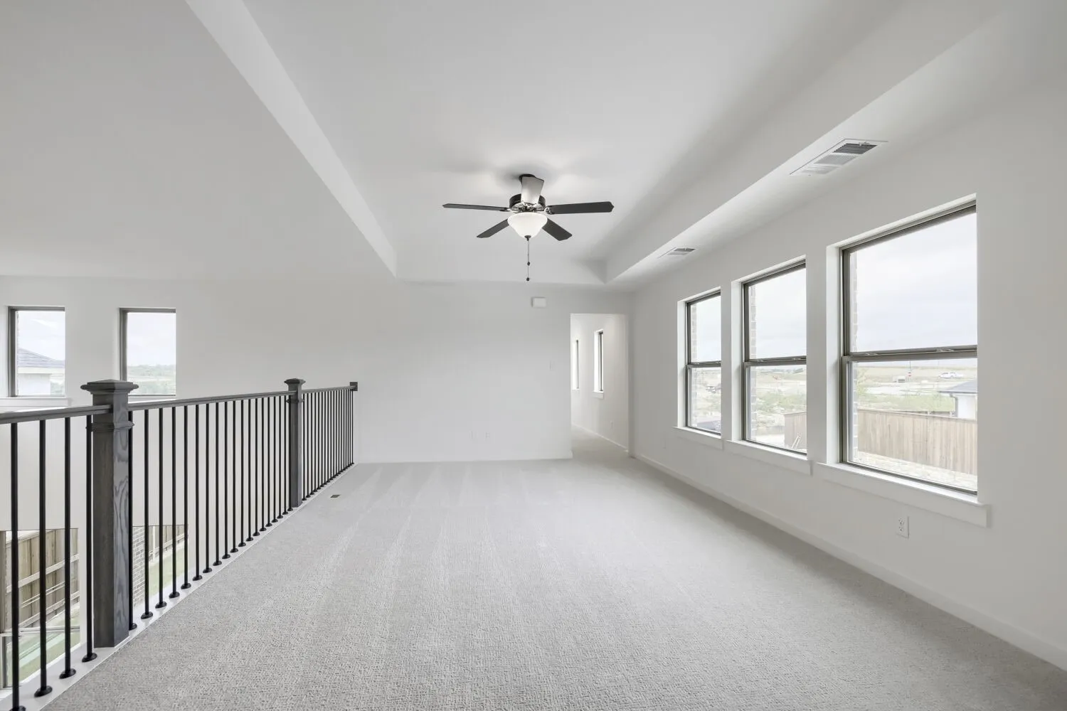Spacious loft area featuring light gray carpeting, a tray ceiling, and a ceiling fan