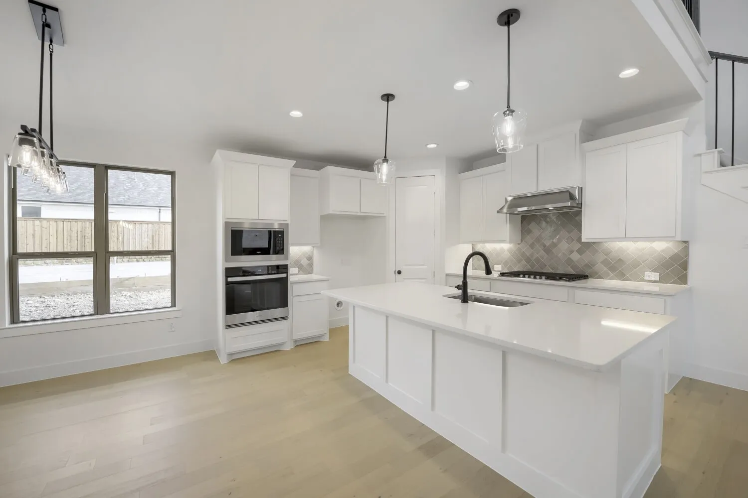 Bright kitchen featuring white cabinetry, a large center island with a sink, stainless steel appliances, light wood-finish flooring, and pendant lighting