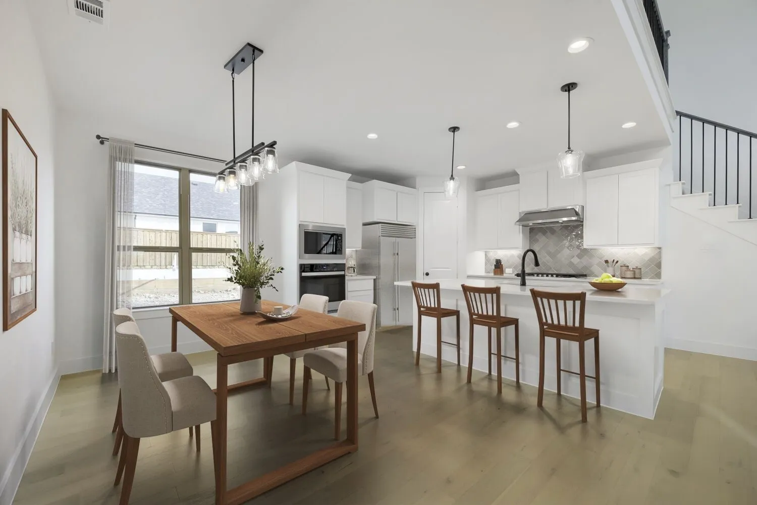 VIRTUALLY STAGED PHOTO Open-concept living area with wood-finish flooring, a contemporary kitchen featuring stainless steel appliances, white cabinetry, and a herringbone tile backsplash, an island with pendant lighting, and a staircase with an open railing