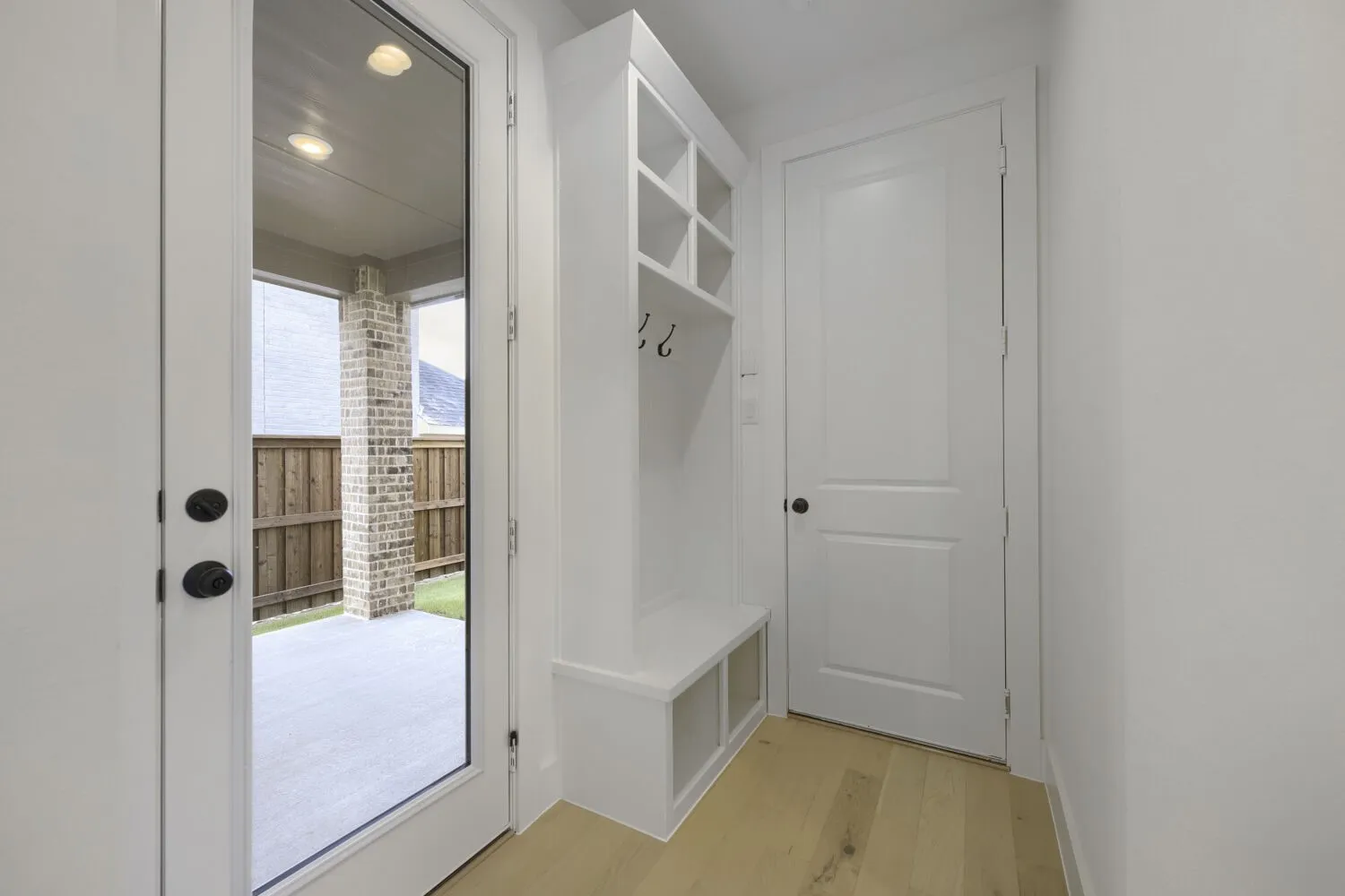 Entryway featuring wood-finish flooring, a white built-in storage bench with cubbies and hooks, and a white paneled interior door