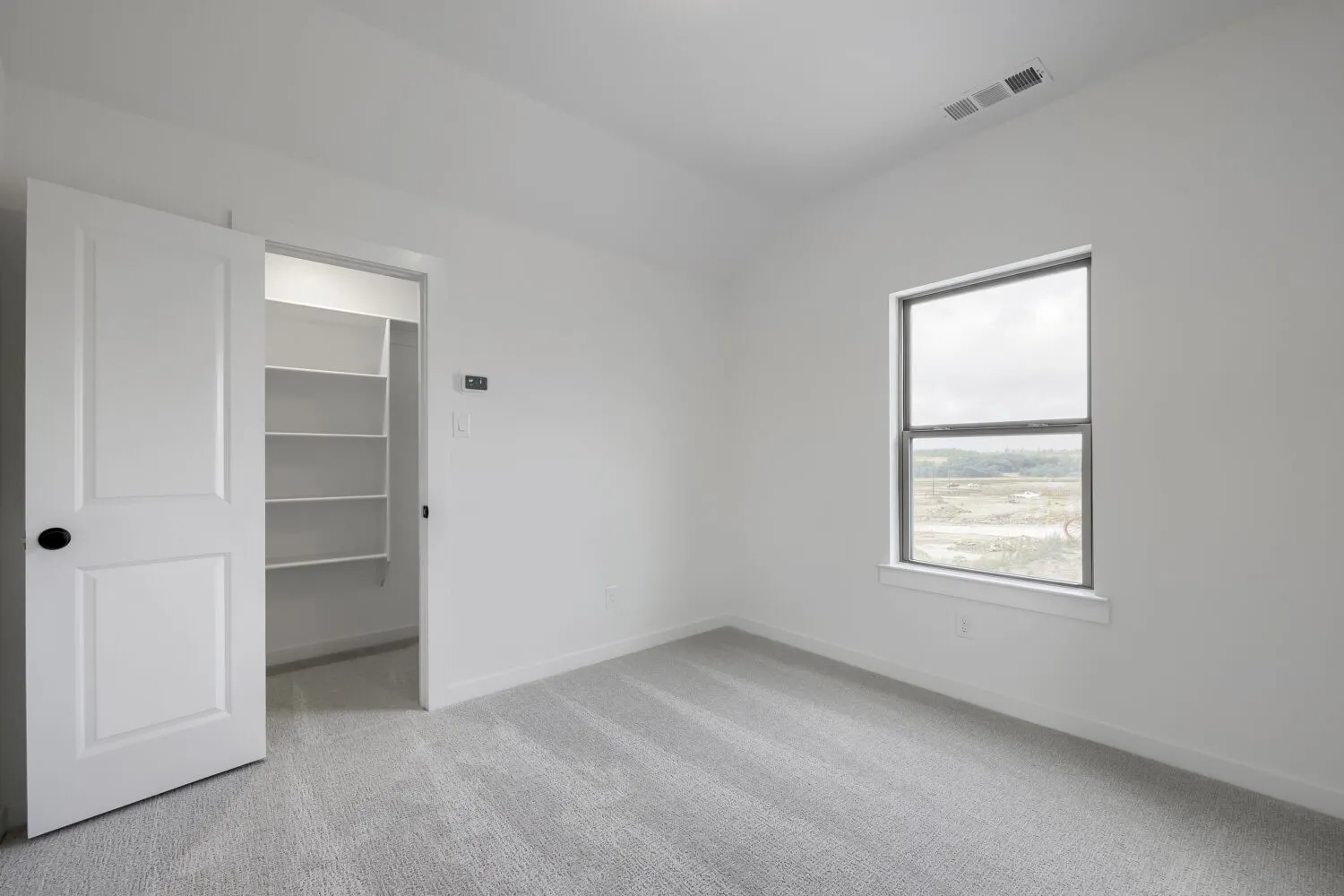 Light-filled room featuring a single window, recessed ceiling vent, light gray carpet, white walls, and a closet with built-in shelving