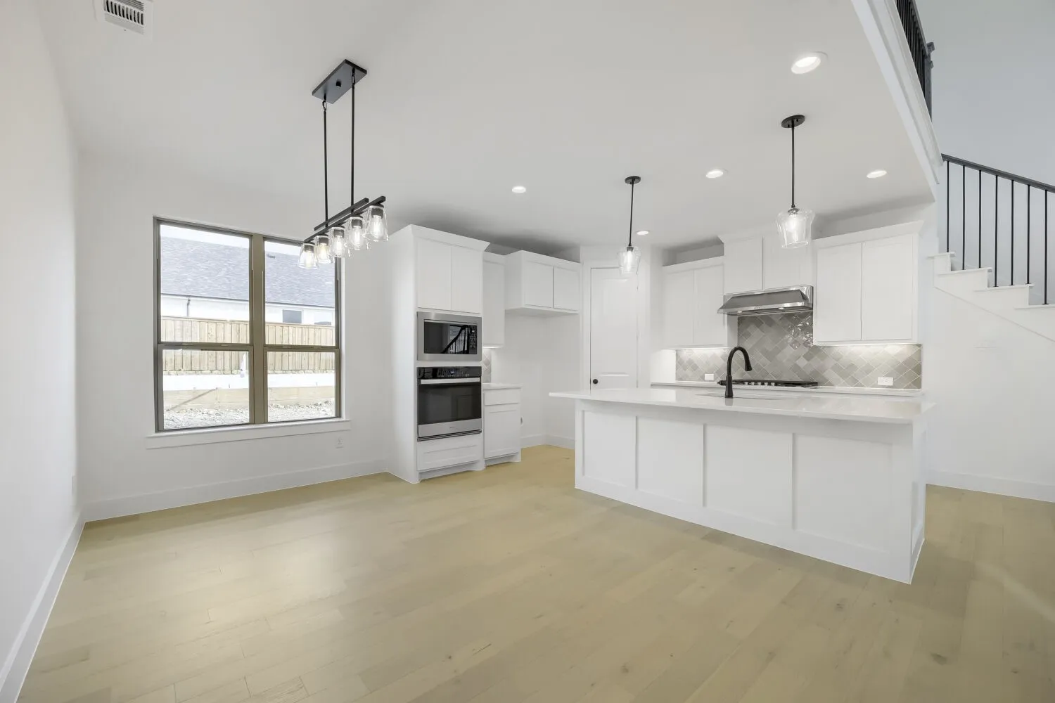 Spacious open-concept kitchen featuring white shaker cabinetry, an expansive island with a light-toned countertop, and integrated stainless steel appliances including a wall oven and microwave