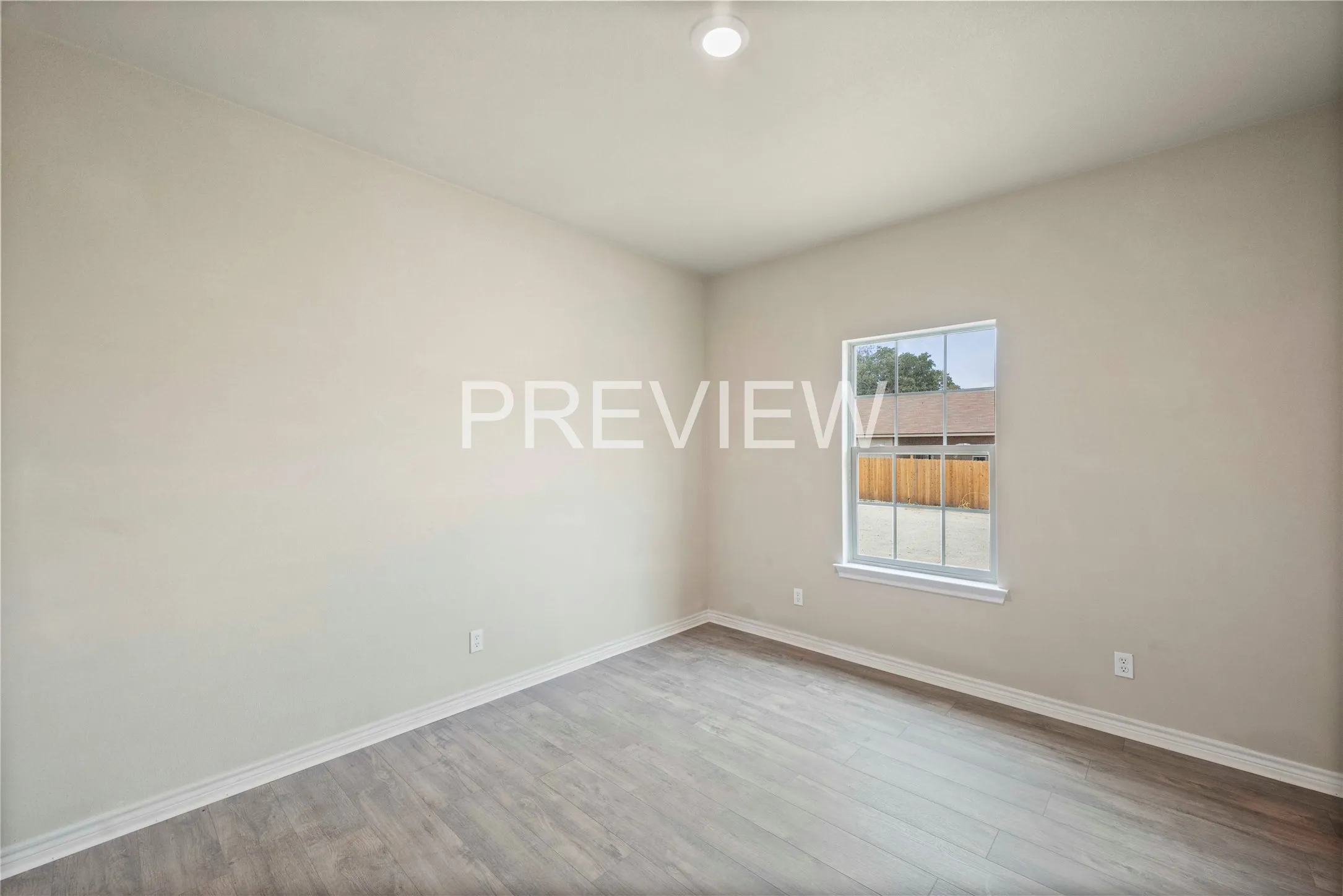 Spacious room featuring wood-finish flooring, light-toned walls, a single window, white baseboards, and an overhead recessed light