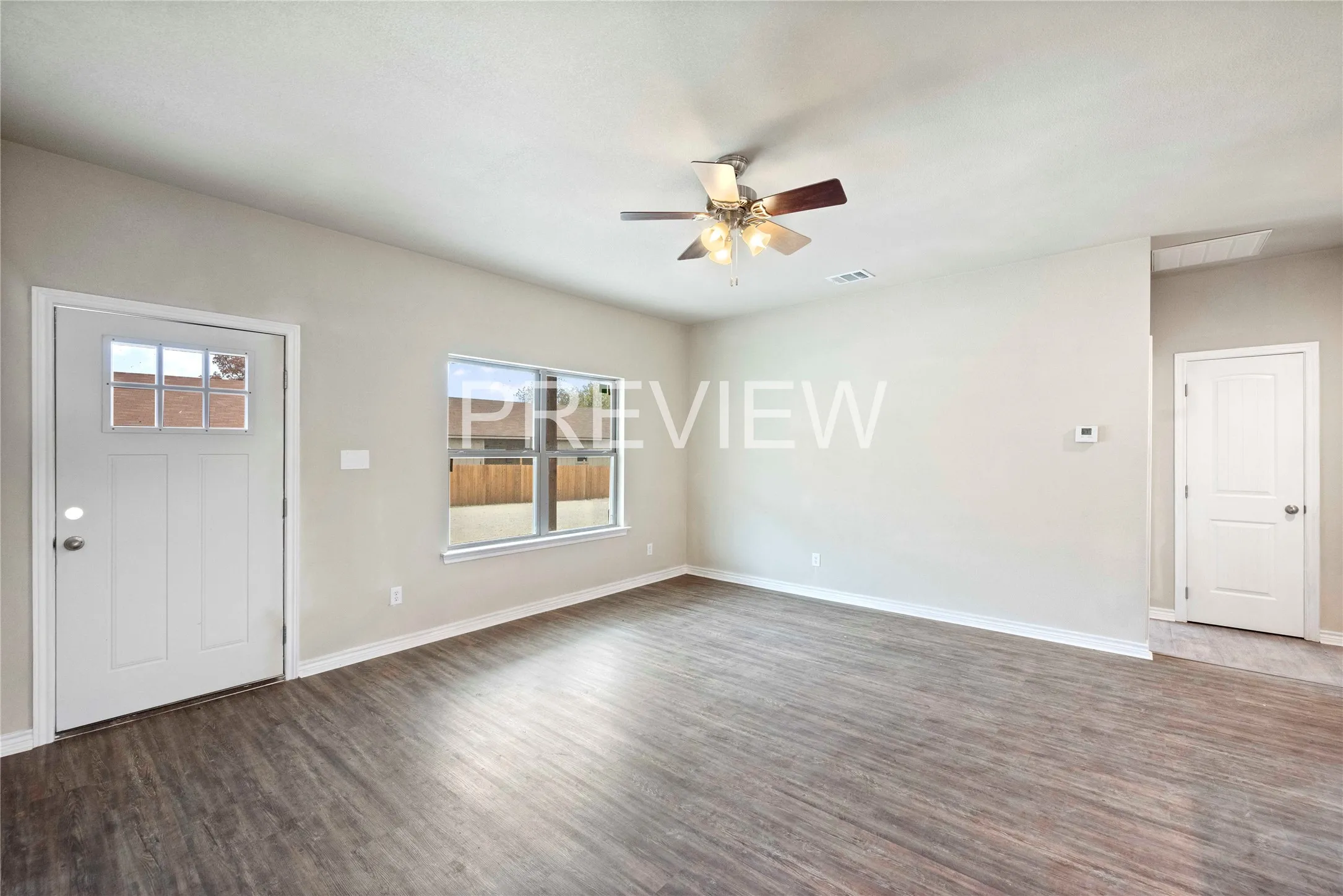 Spacious room featuring wood-finish flooring, light neutral wall tones, a ceiling fan with integrated lighting, and multiple windows