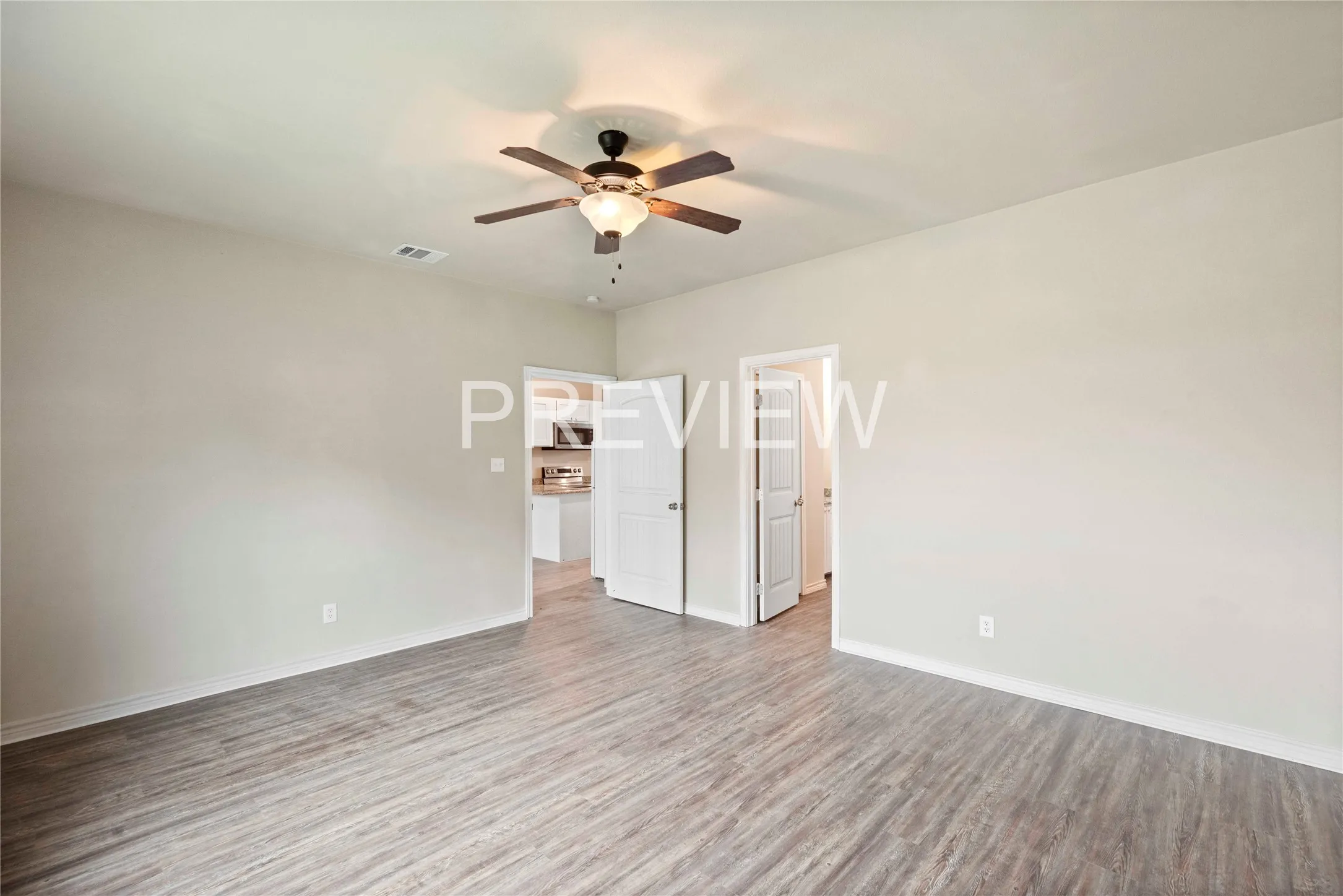 Spacious room featuring wood-finish flooring, a ceiling fan with integrated lighting, and light-toned wall finishes
