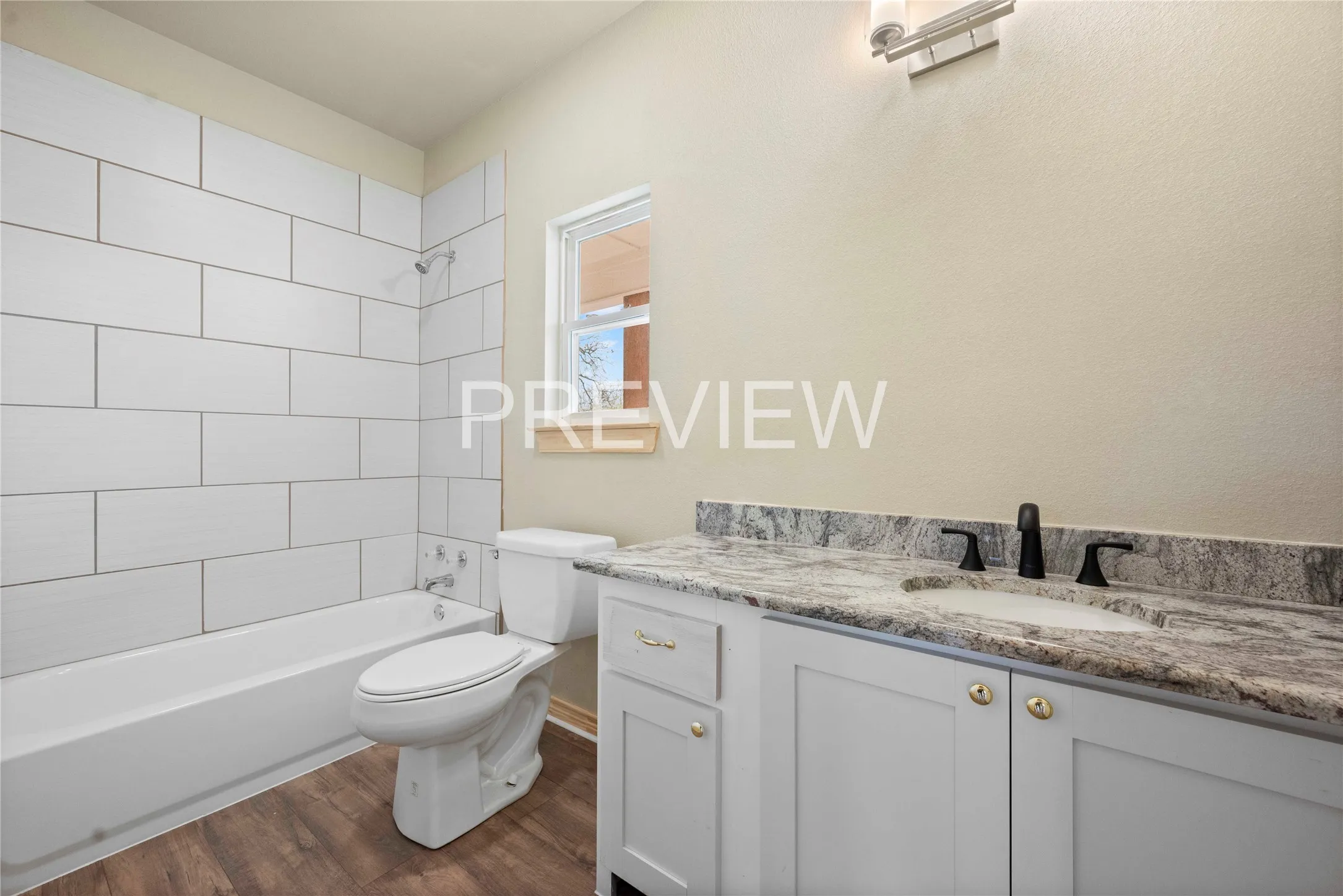 Bathroom featuring white subway tile tub surround, wood-finish flooring, white vanity with gold-tone hardware, integrated sink, and black fixtures