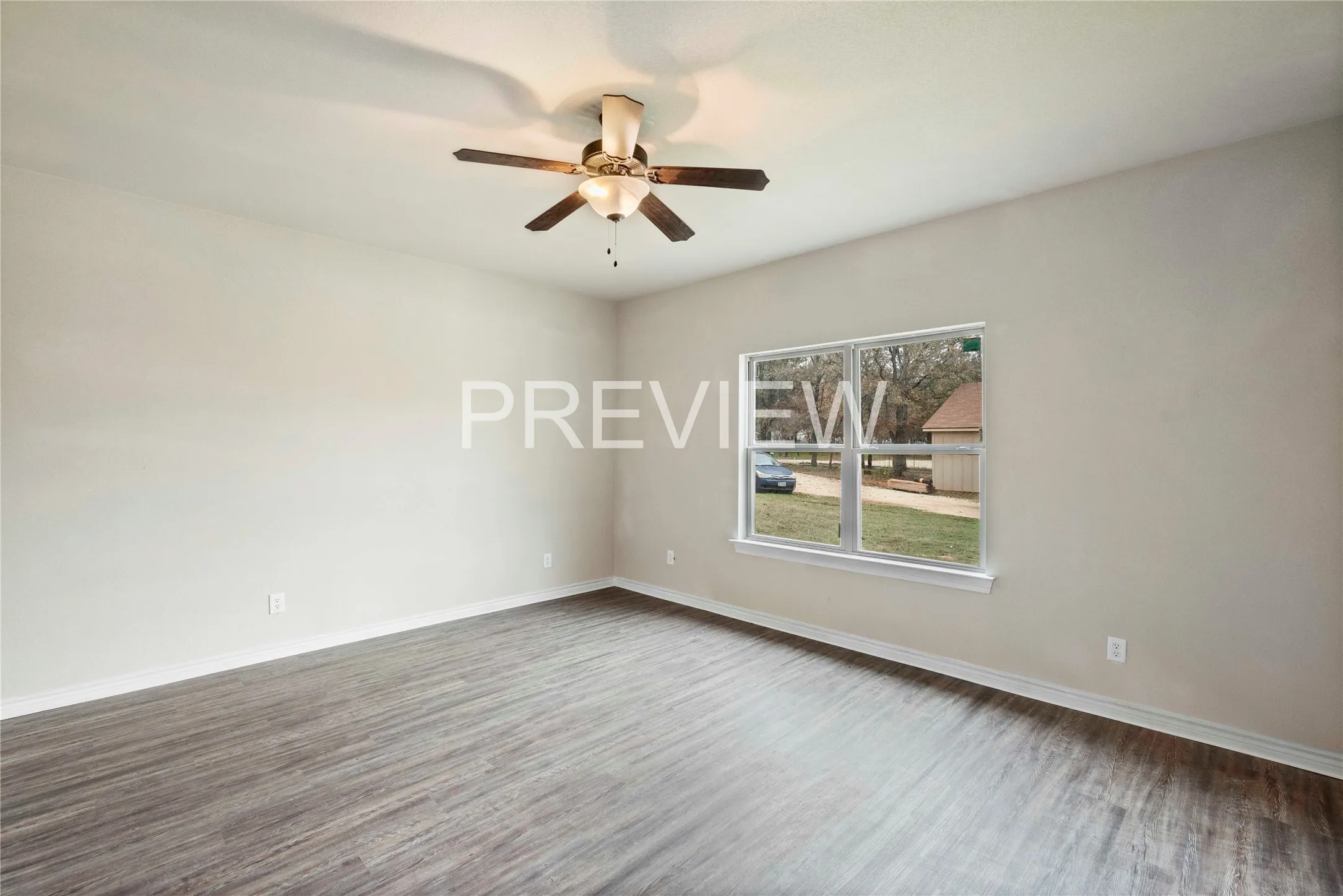 Spacious room featuring wood-finish flooring, a ceiling fan with integrated lighting, a large window with white trim, and neutral wall paint