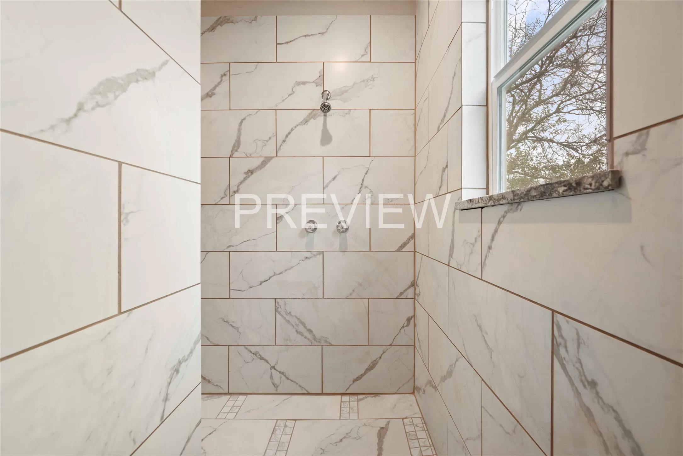 Spacious shower area featuring large format white tile with gray veining, dual shower heads, and a built-in window with a stone sill