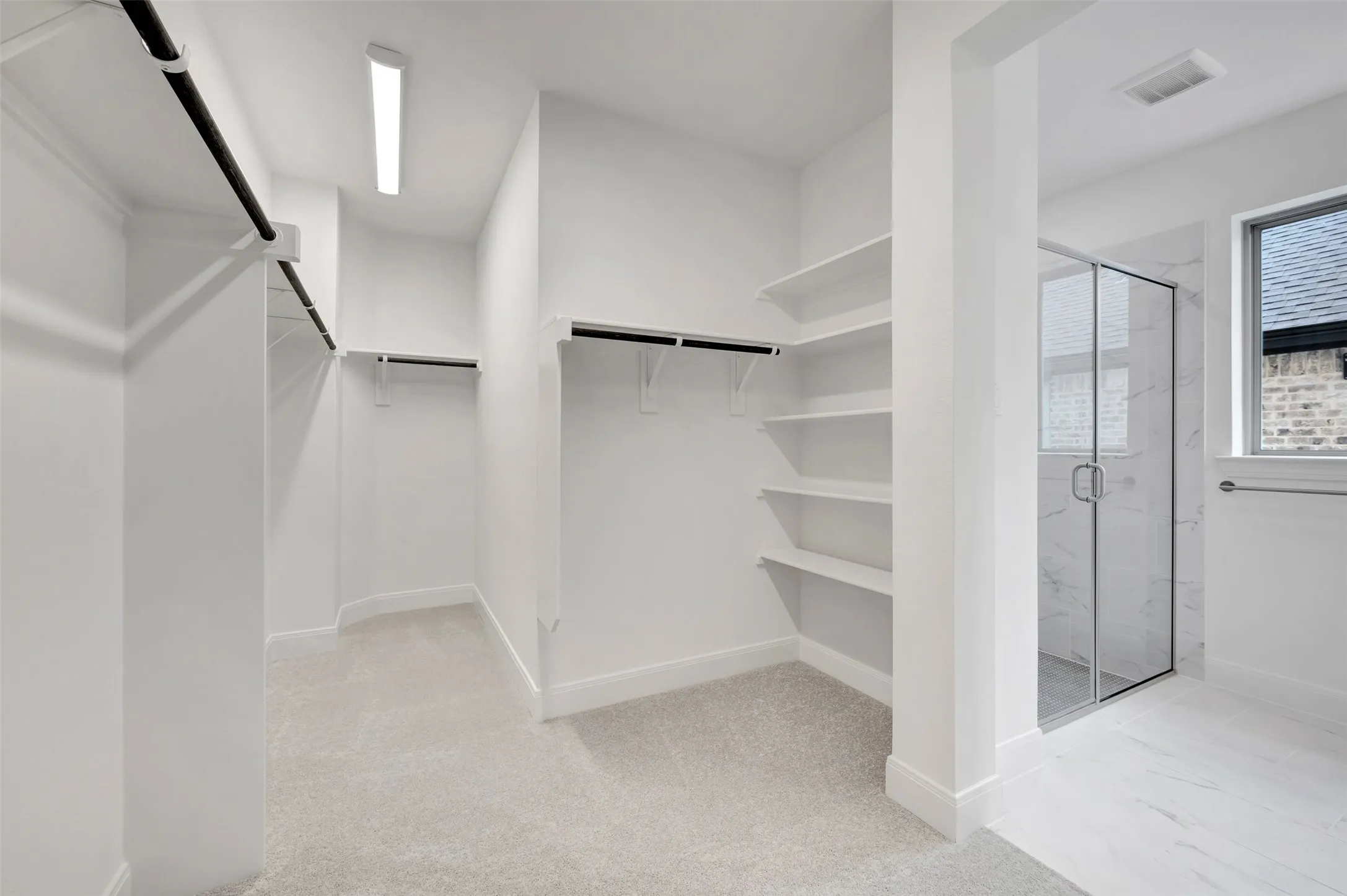 Spacious walk-in closet featuring multiple clothing rods, built-in shelving throughout, polished concrete flooring, and abundant natural light from skylights