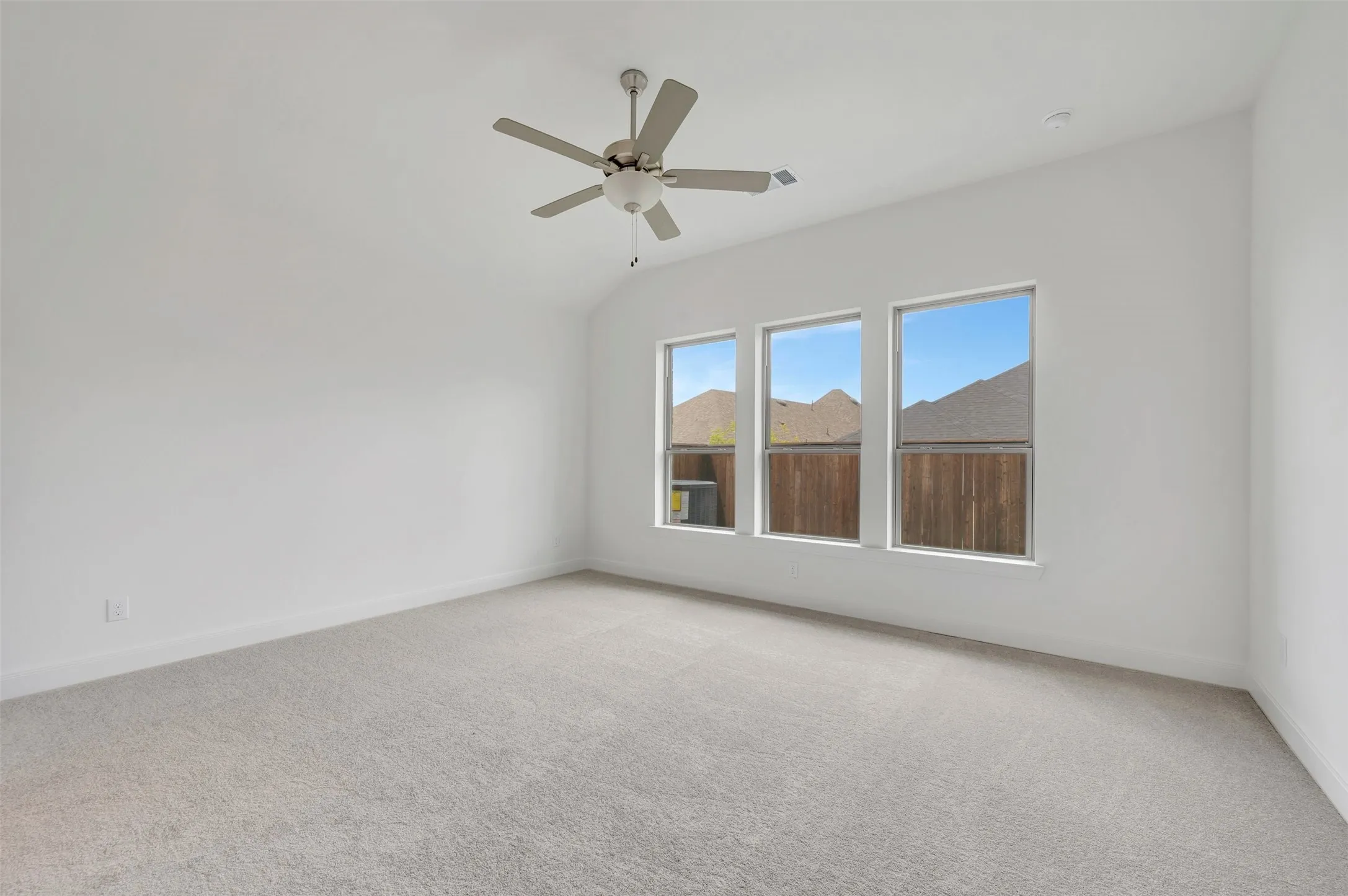 Vaulted ceiling with a ceiling fan, three large windows, and neutral carpeting