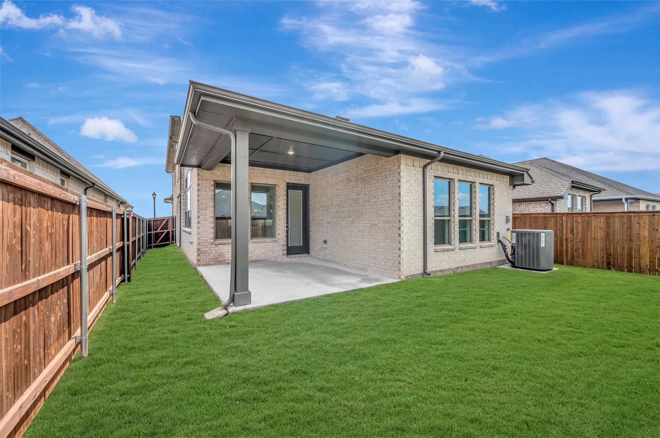 Brick exterior with covered patio, concrete slab, and a green lawn