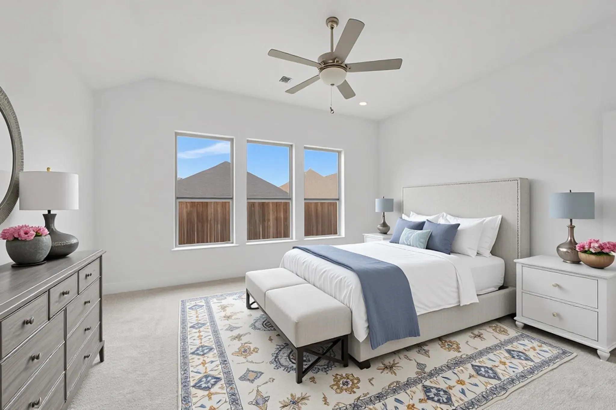 Bright, light-filled primary bedroom with expansive multi-pane windows framing mountain vistas, neutral wall finishes, hardwood flooring, ceiling fan with integrated lighting, and coordinating nightstands with task lighting on either side of the bed frame