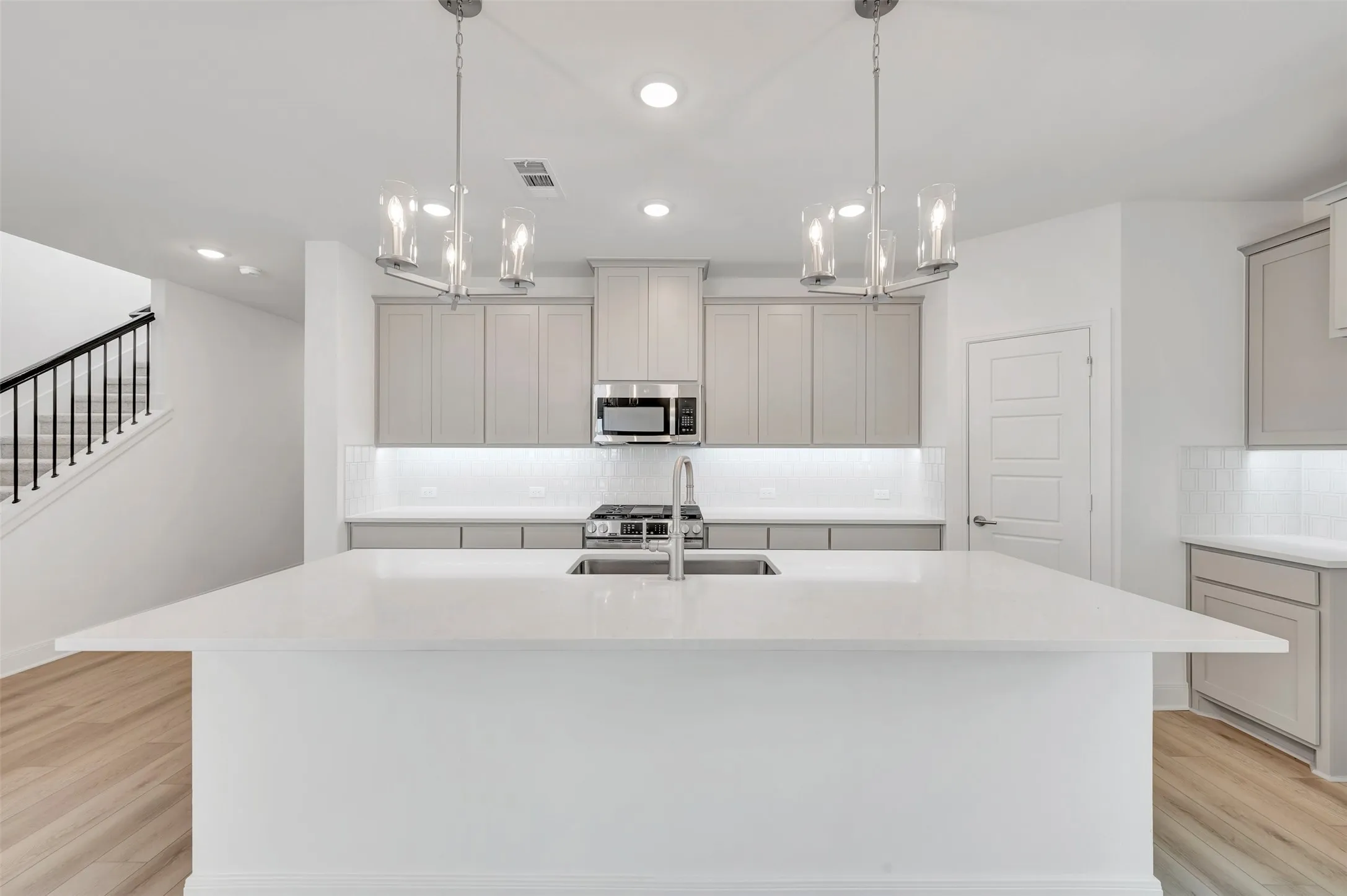 Spacious kitchen island with a built-in sink, stainless steel appliances, light-toned cabinetry, subway tile backsplash, and wood-finish flooring