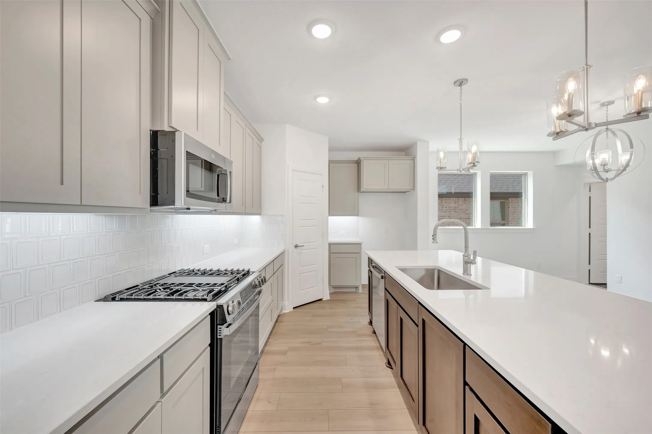Kitchen featuring recessed lighting, light wood-finish flooring, a stainless steel gas range, an under-mount sink, and dual pendant lighting fixtures
