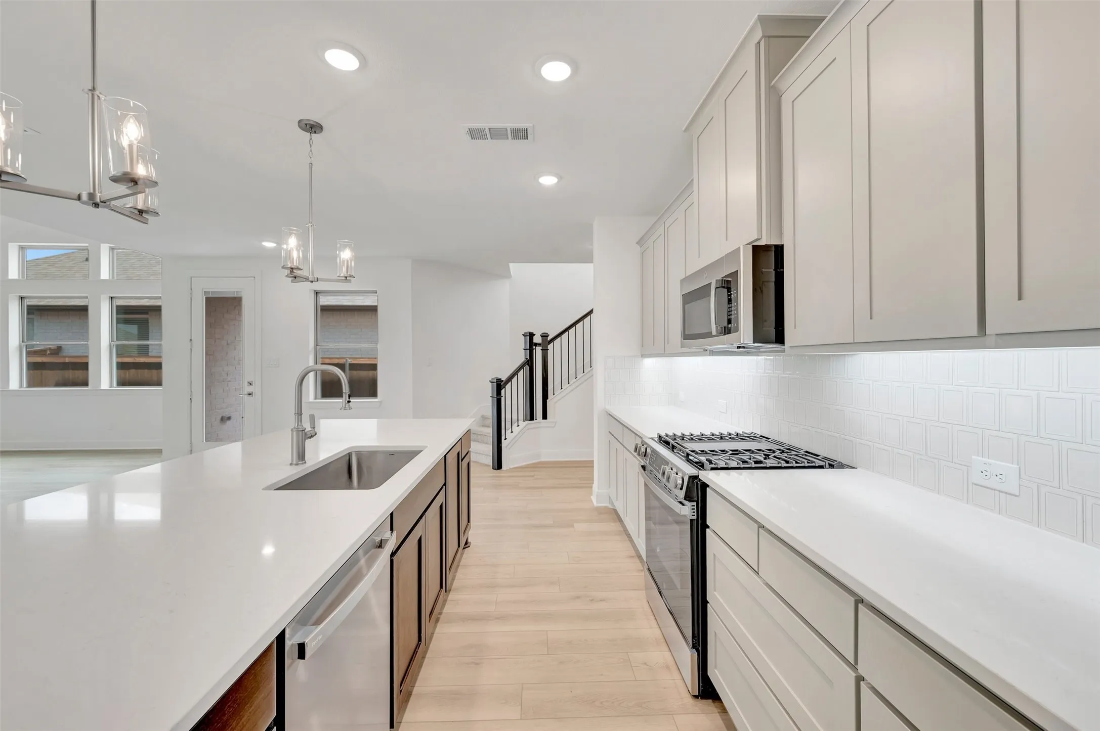 Kitchen featuring a large central island with an undermount sink, light-toned cabinetry, stainless steel appliances, a tile backsplash, and recessed lighting