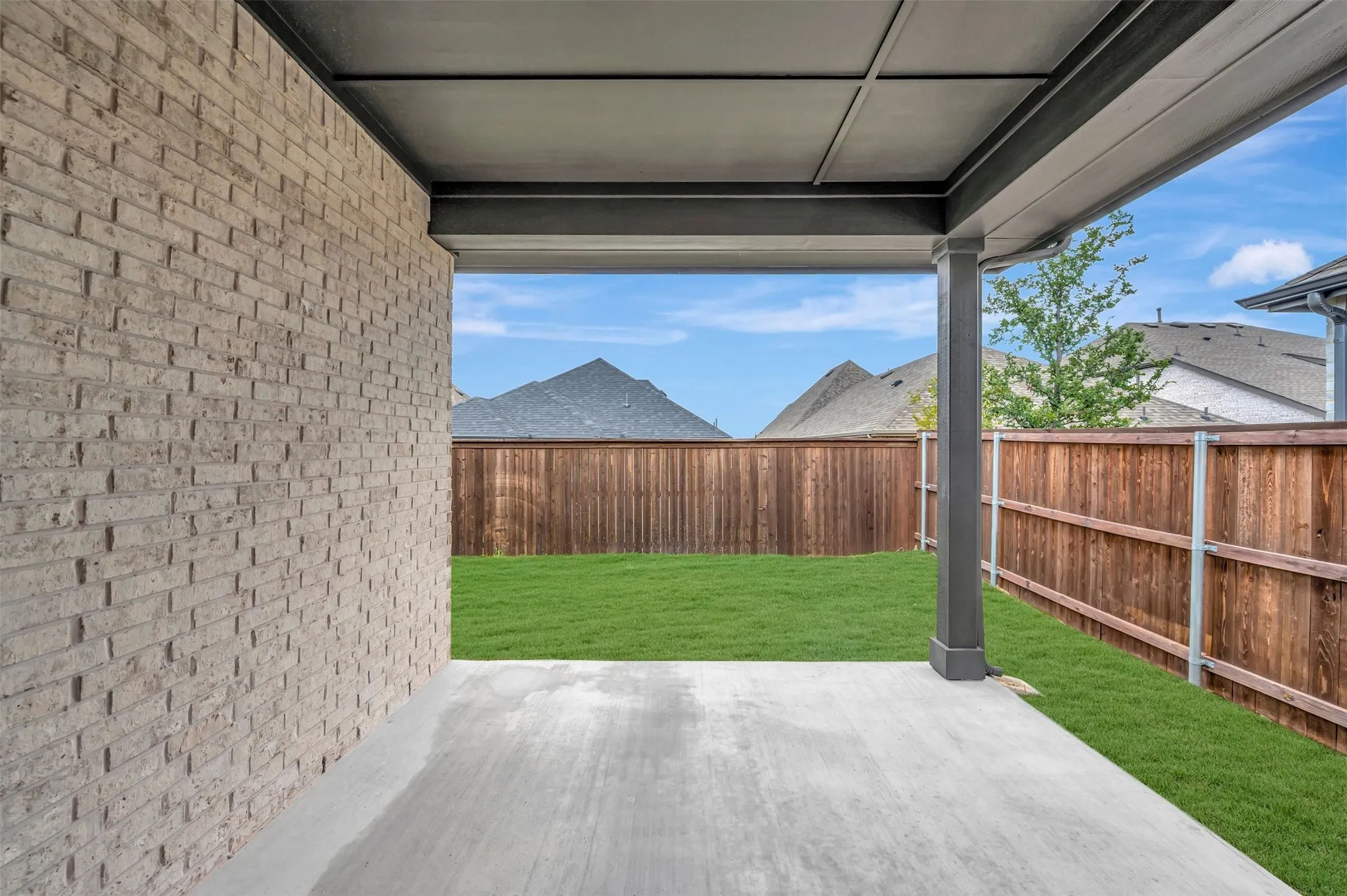 Covered patio with a concrete surface, expansive lawn, wood fencing, and brick exterior