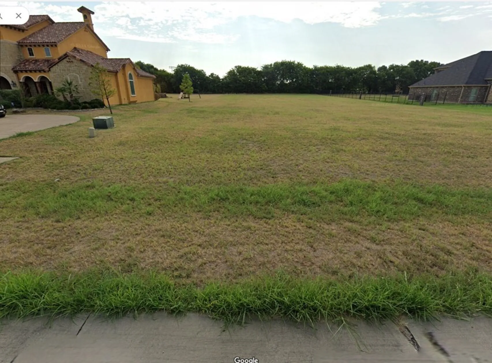 Expansive lot featuring a large grassy area and a paved driveway entrance, offering ample space