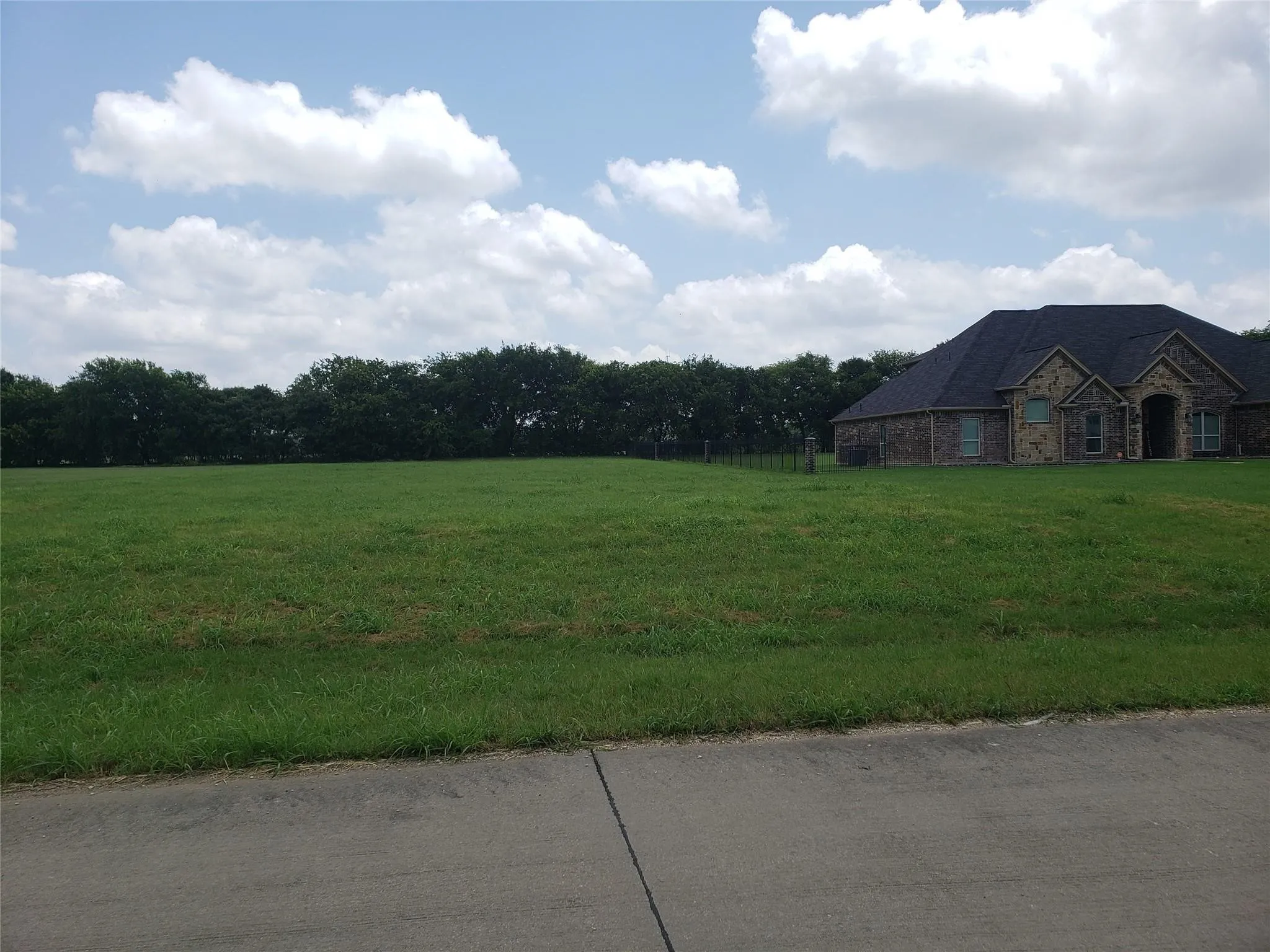 Expansive green lawn with a tree line in the background and a portion of a brick property visible on the right