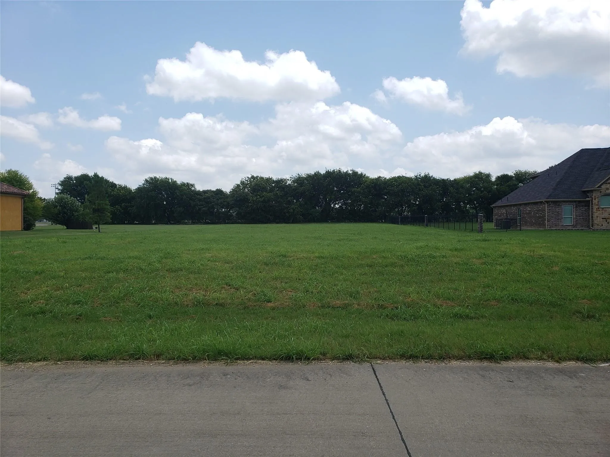 Expansive green lawn with mature trees in the background, set under a sky with visible clouds