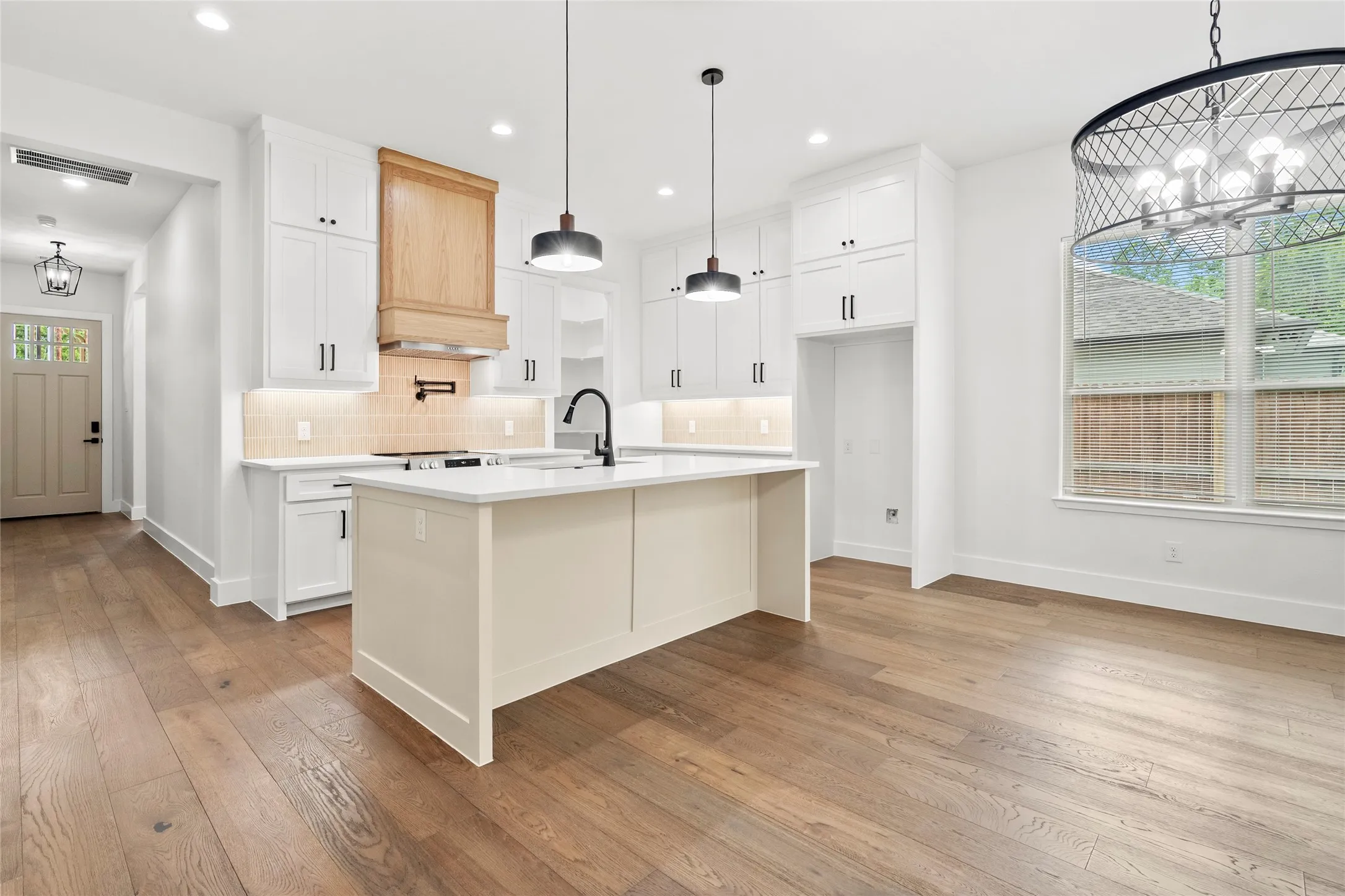 Open-concept kitchen and dining area featuring wide plank wood-finish flooring, white shaker cabinetry, a central island, and a decorative chandelier