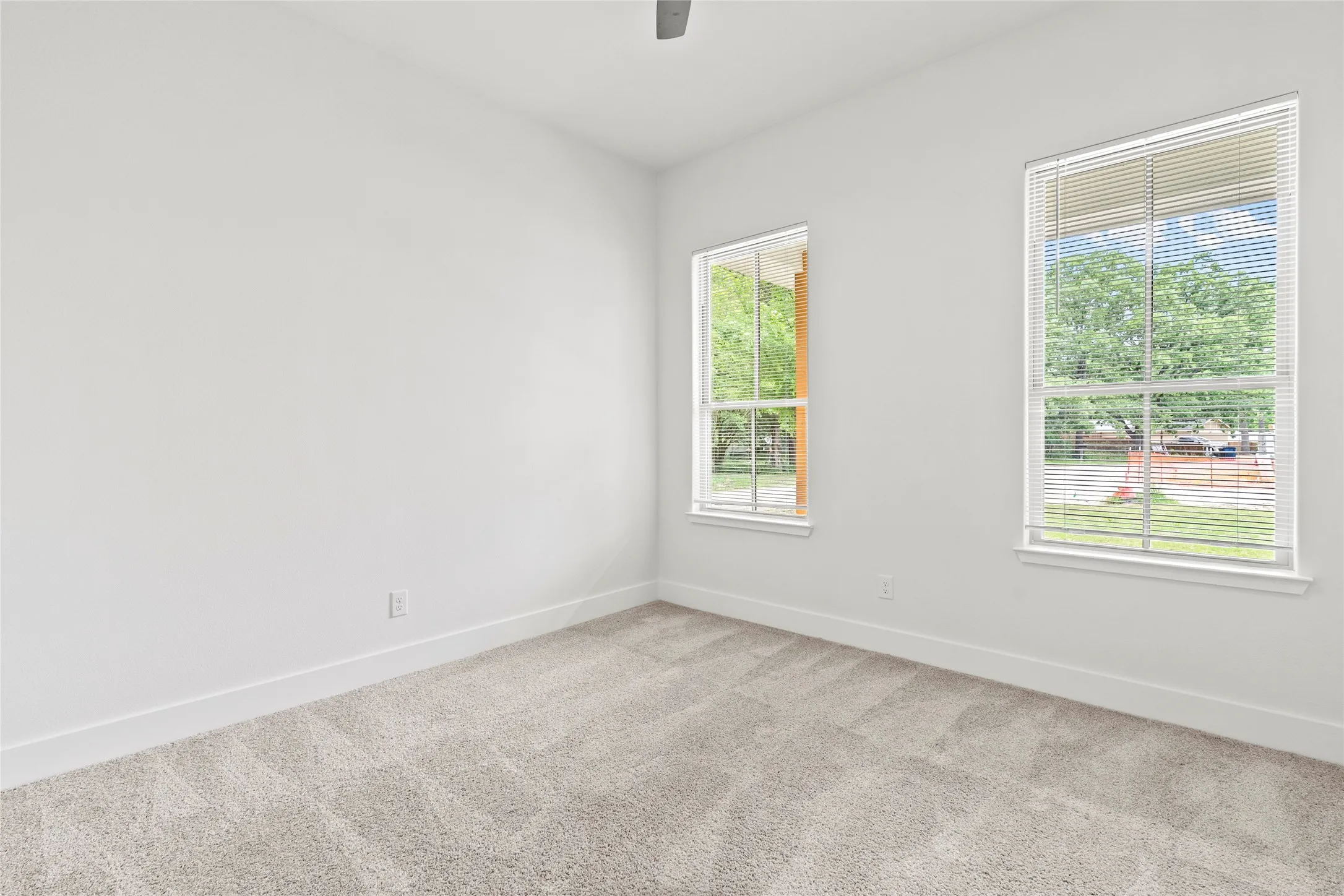 Carpeted room featuring two windows with horizontal blinds, white walls, and a ceiling fan