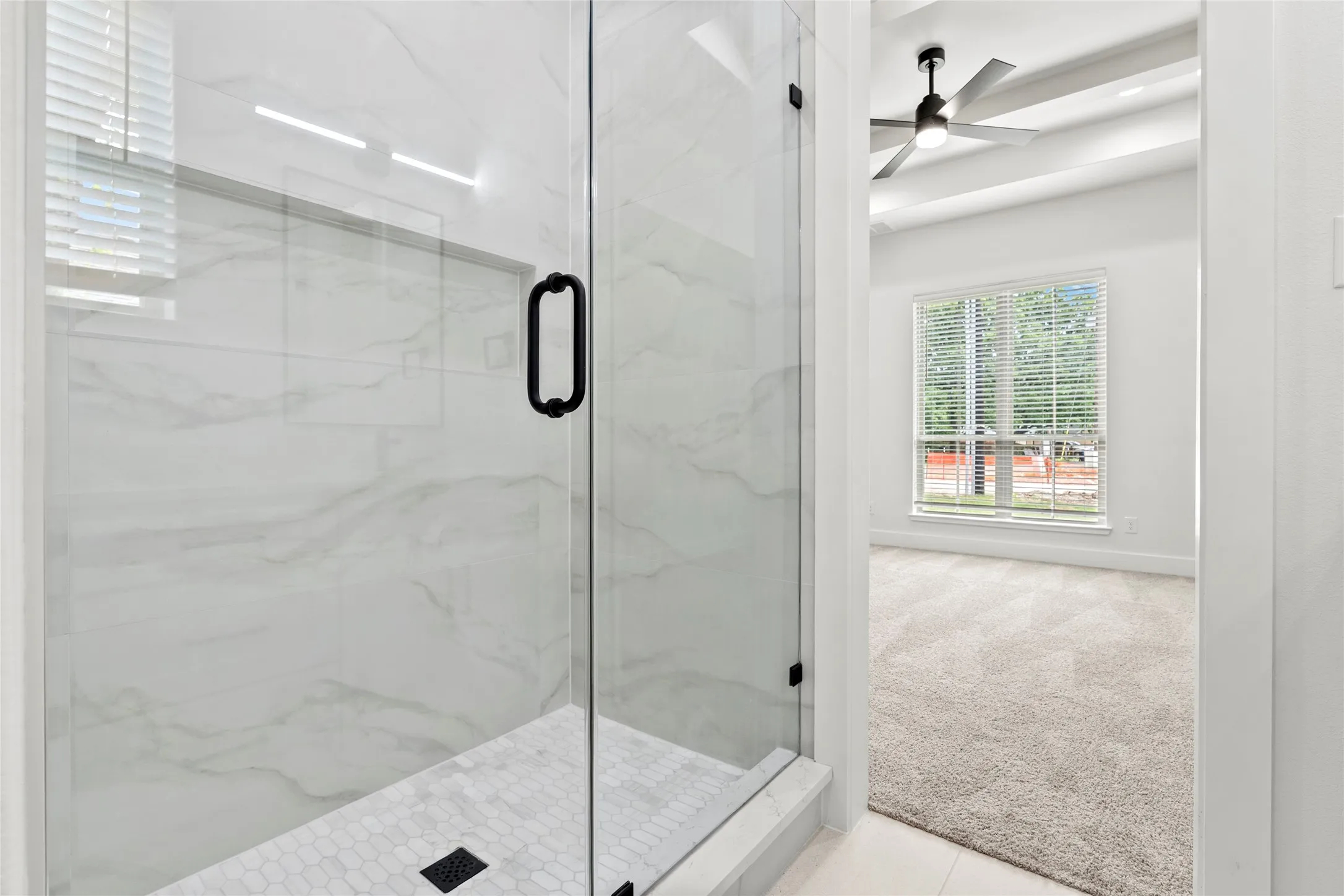 Glass-enclosed shower featuring white marble-look tile walls and a hexagonal tile floor