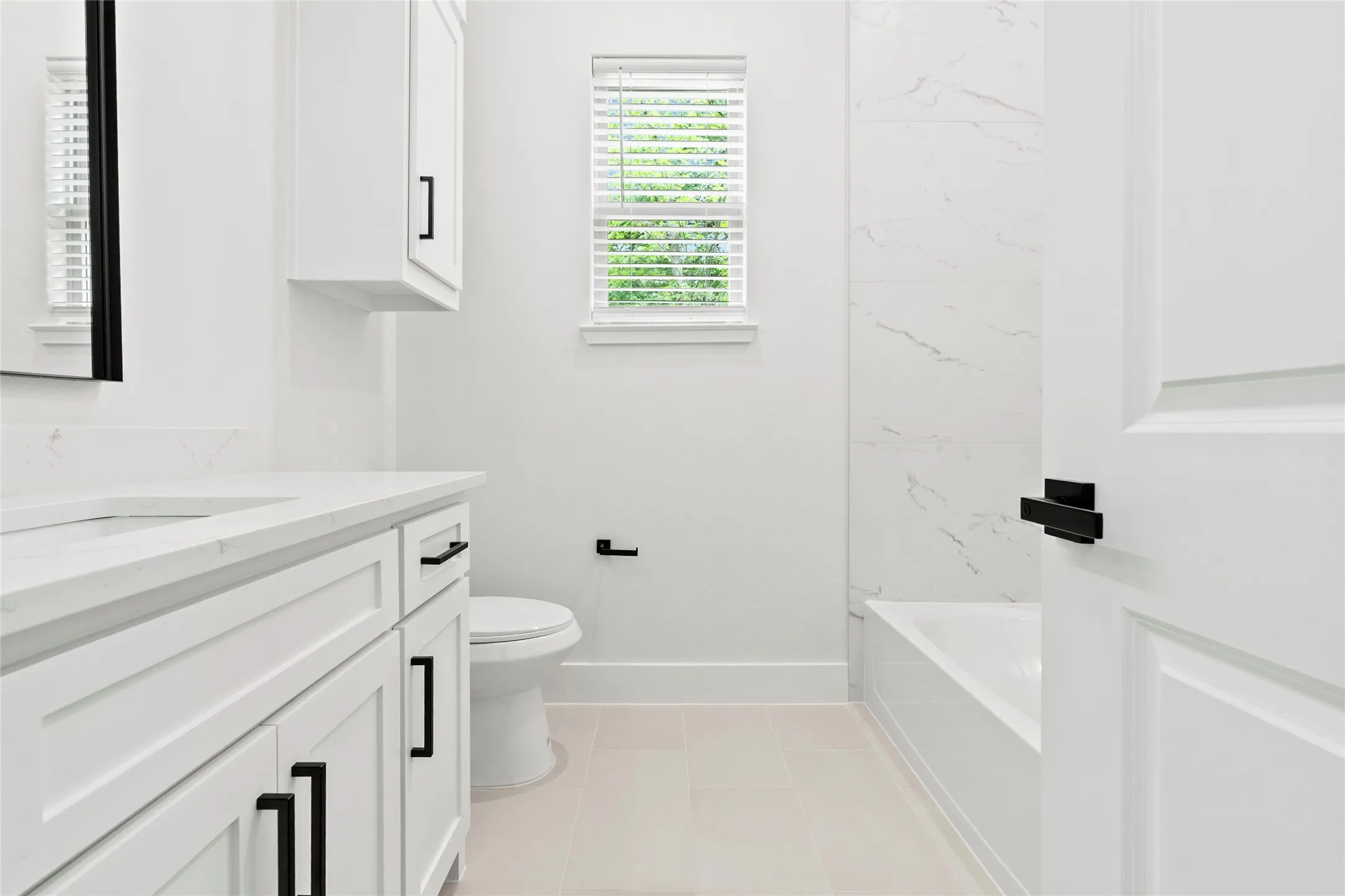 Bathroom featuring a white vanity with quartz countertop, integrated sink, and black hardware