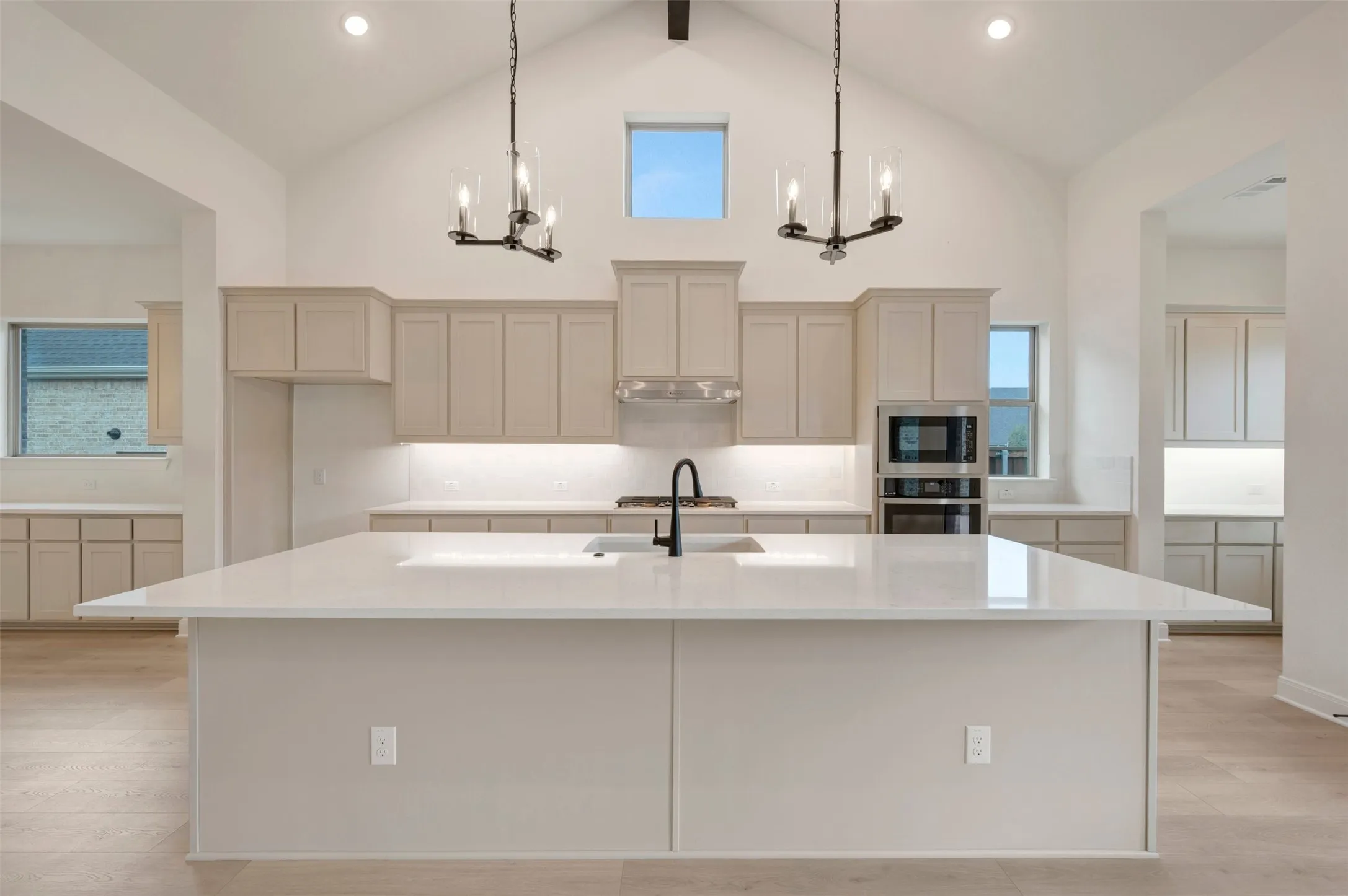 Vaulted ceiling with exposed beam, dual chandeliers, large center island with integrated sink, built-in oven and microwave, and extensive cabinetry with under-cabinet lighting